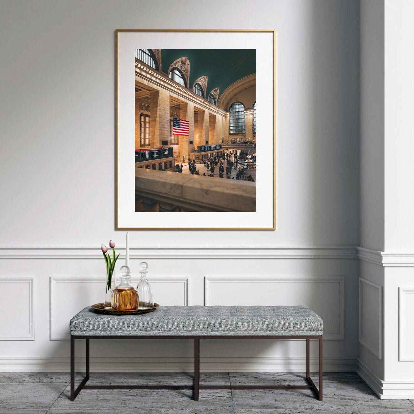 A Grand Central framed photo hangs above a bench in a minimalist room with a decanter and glass.