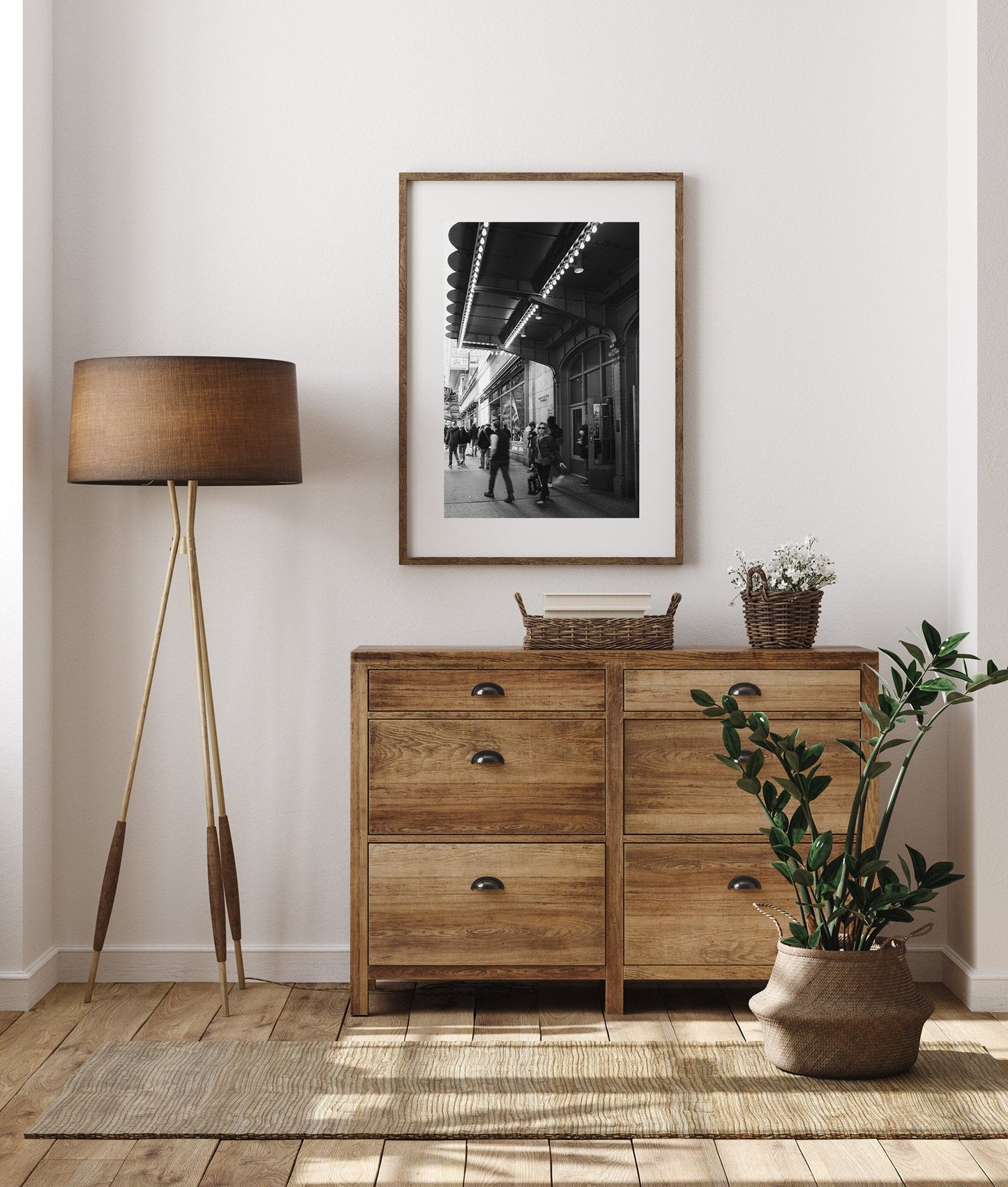 Cozy room with a wooden dresser, a lamp, a plant, and a Grand Central Rhythm Black and White photo on the wall.