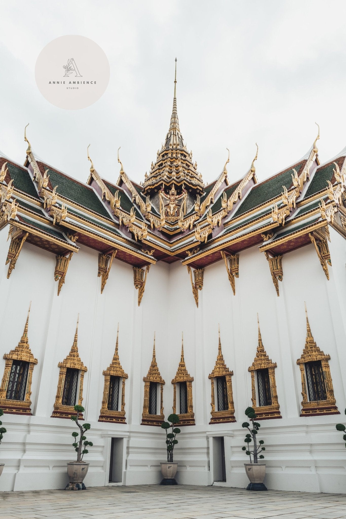 Grand Palace VI with gold detailing and spires, under cloudy skies, surrounded by potted plants.