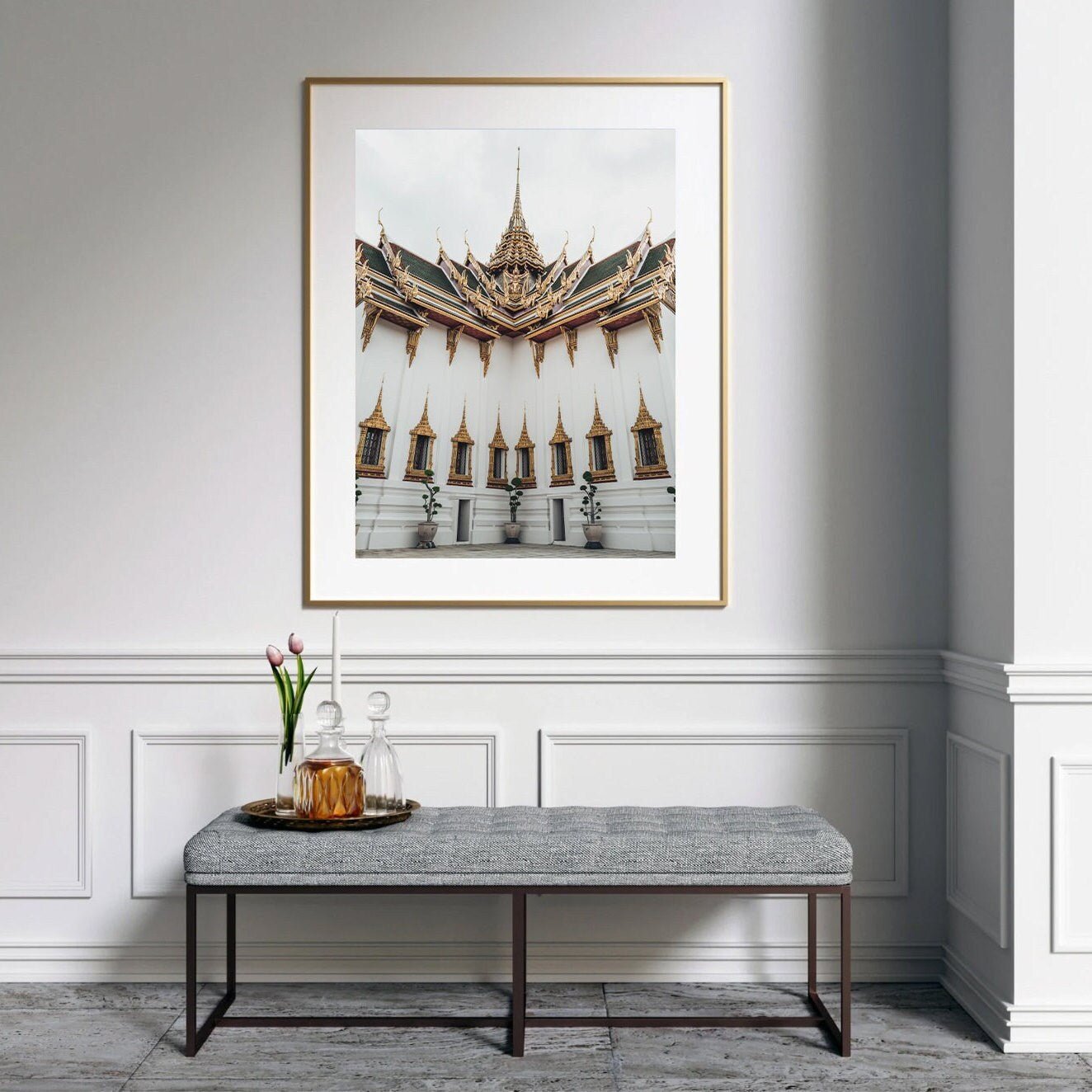 A minimalist room featuring the Grand Palace VI photo, a bench below, and a vase with tulips and a glass decanter set.