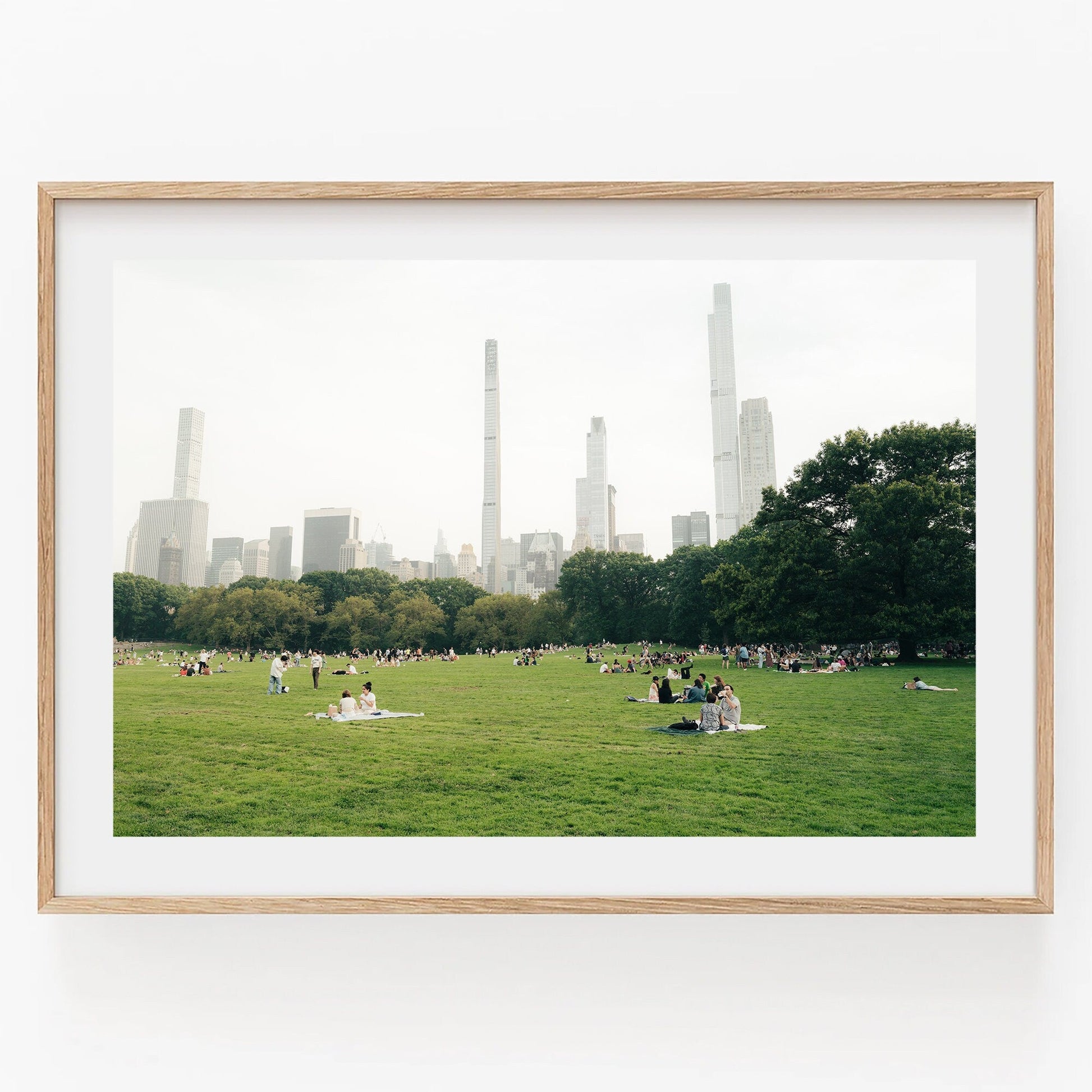 People relaxing on Great Lawn in a park with tall buildings in the background under a cloudy sky.