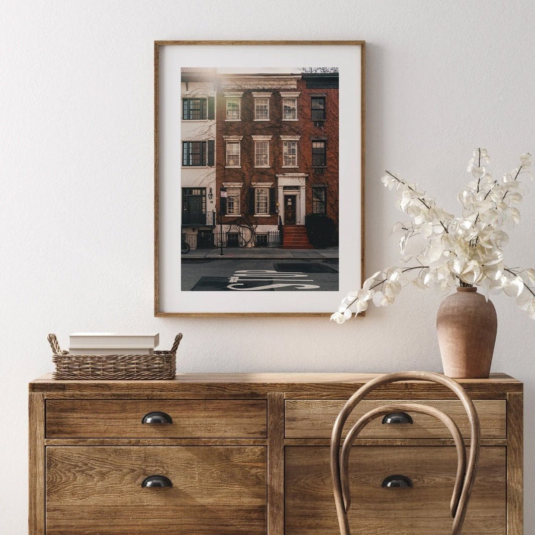 The Grove Street photo of a brick building hangs above a wooden dresser with a vase and wicker basket.