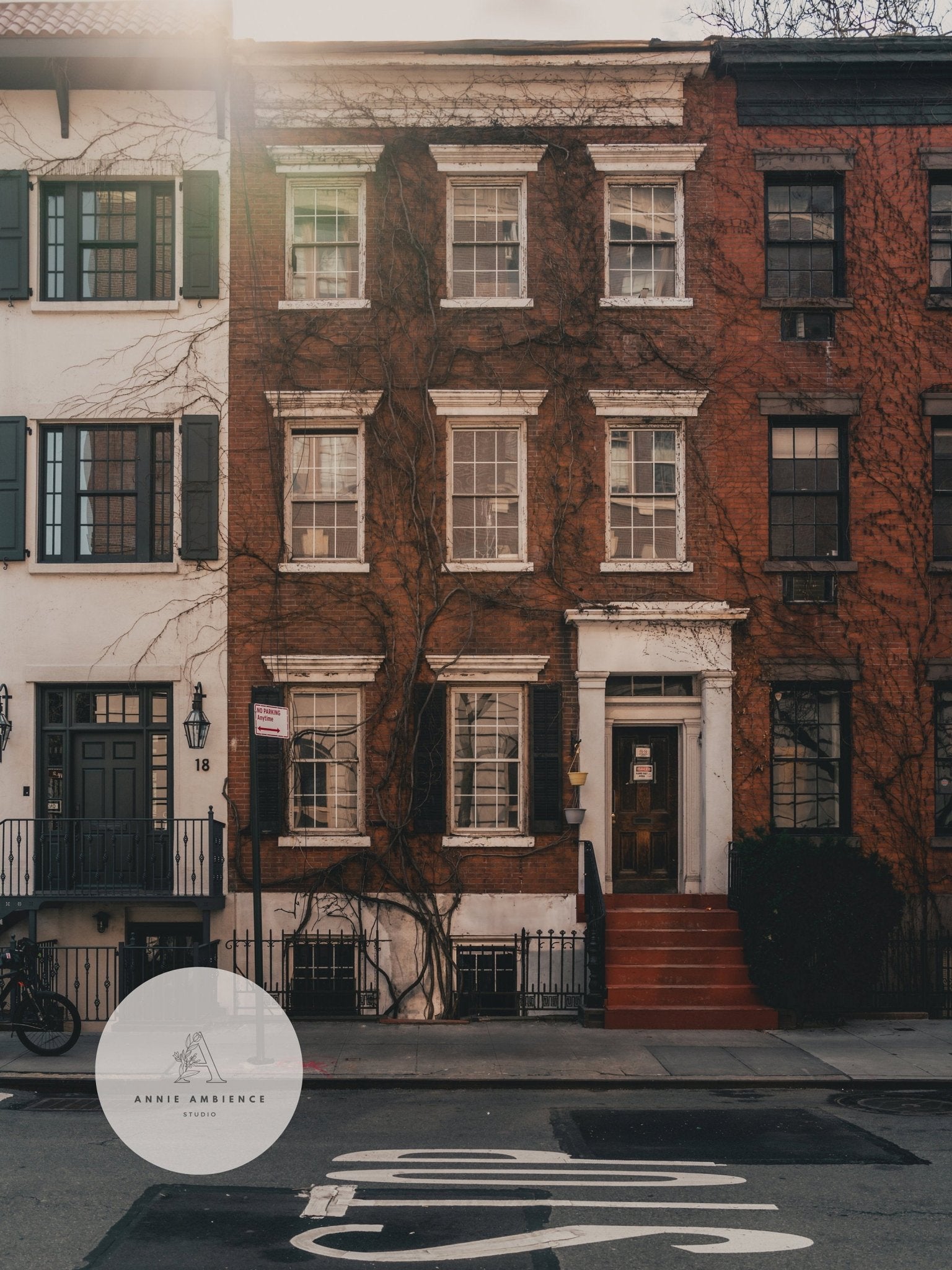 Street view of Grove Street brick townhouse with ivy, near a white building. Sunlight filters from top left.