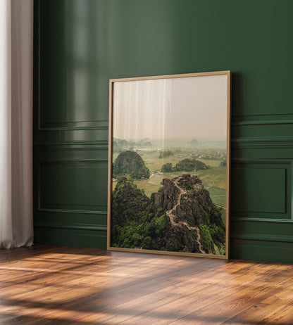 Hang Mua Peak I landscape painting leans against a dark green wall on a wooden floor.