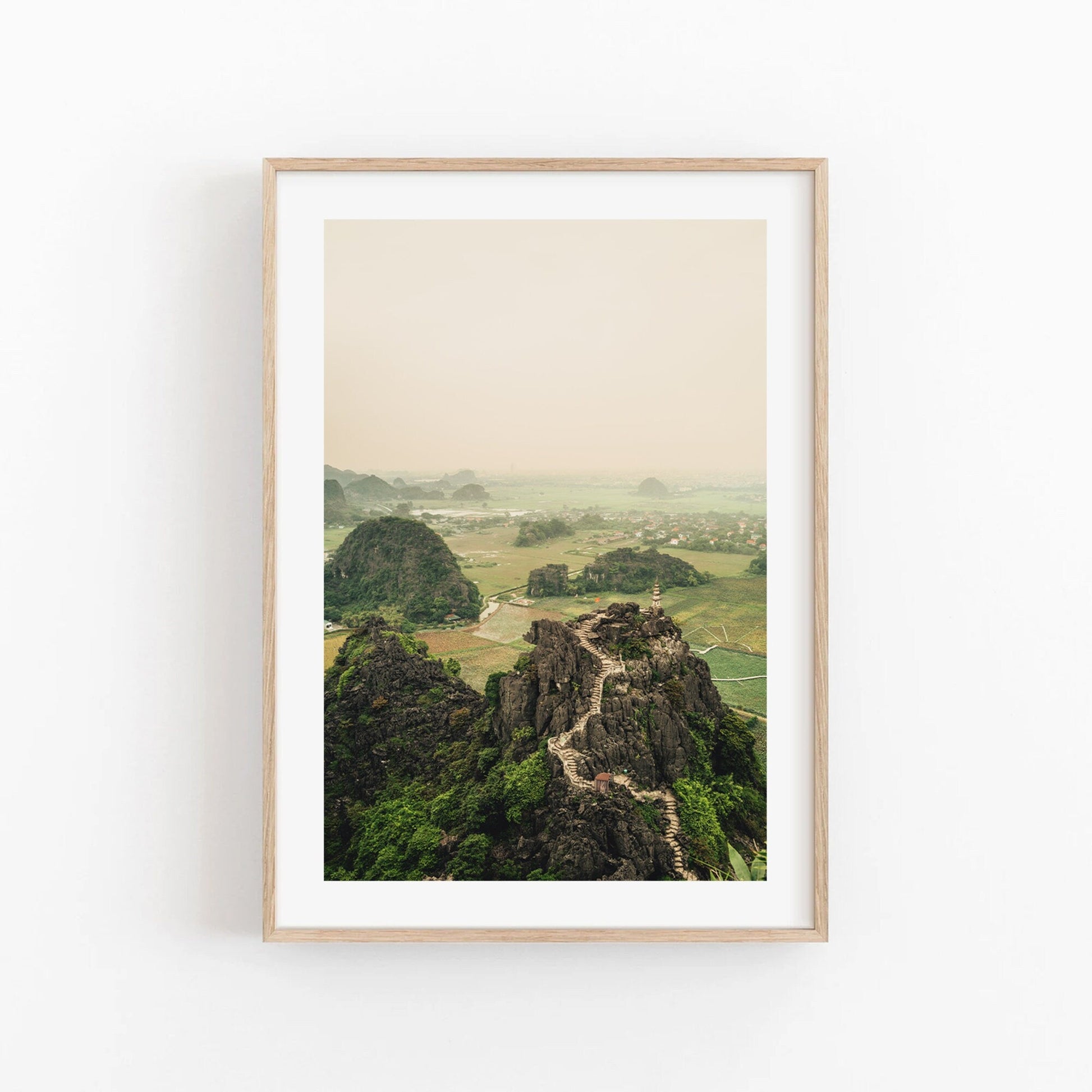 Framed photograph of Hang Mua Peak with rocky hills and fields under a hazy sky.