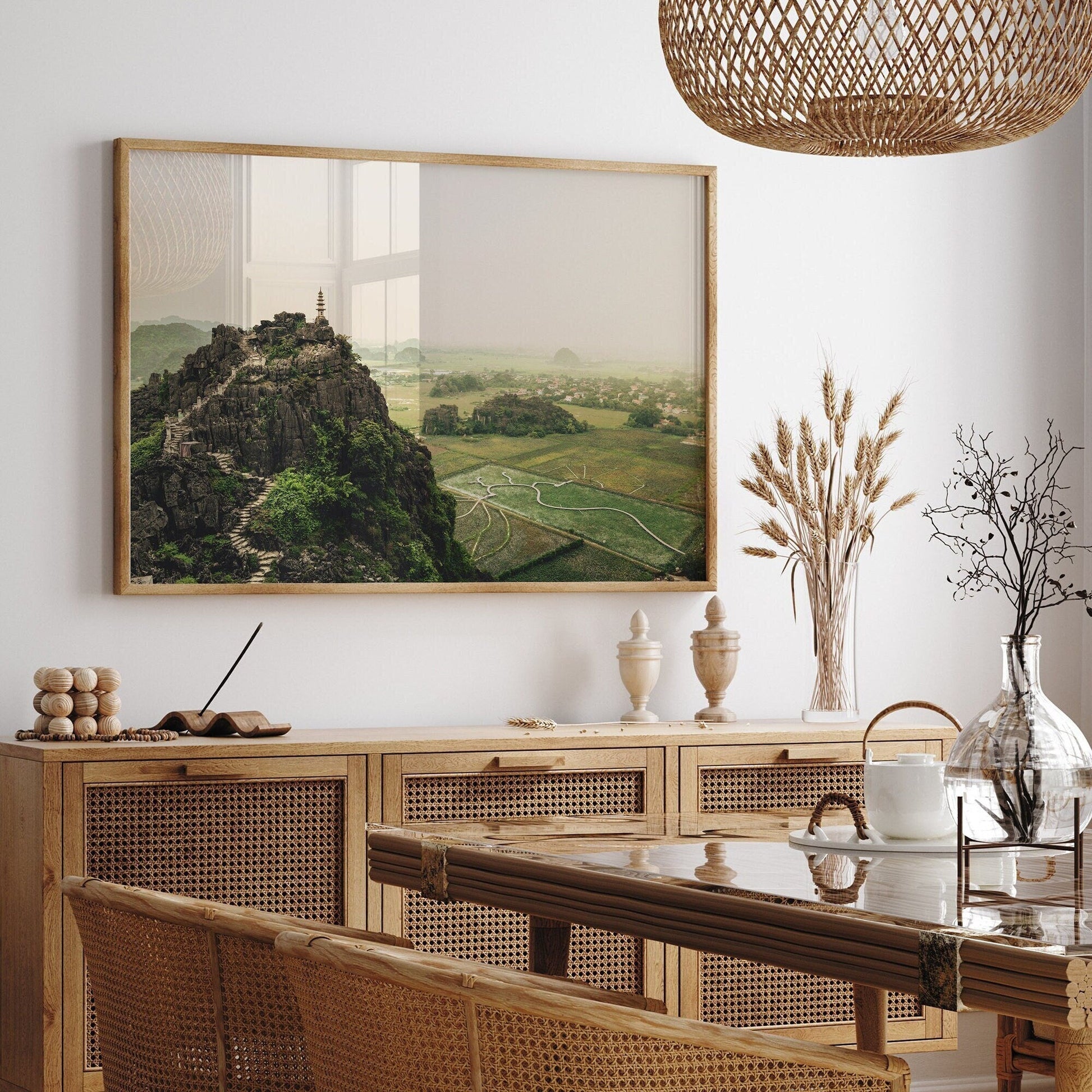 A dining room with wicker furniture and a landscape painting of Hang Mua Peak II on the wall.