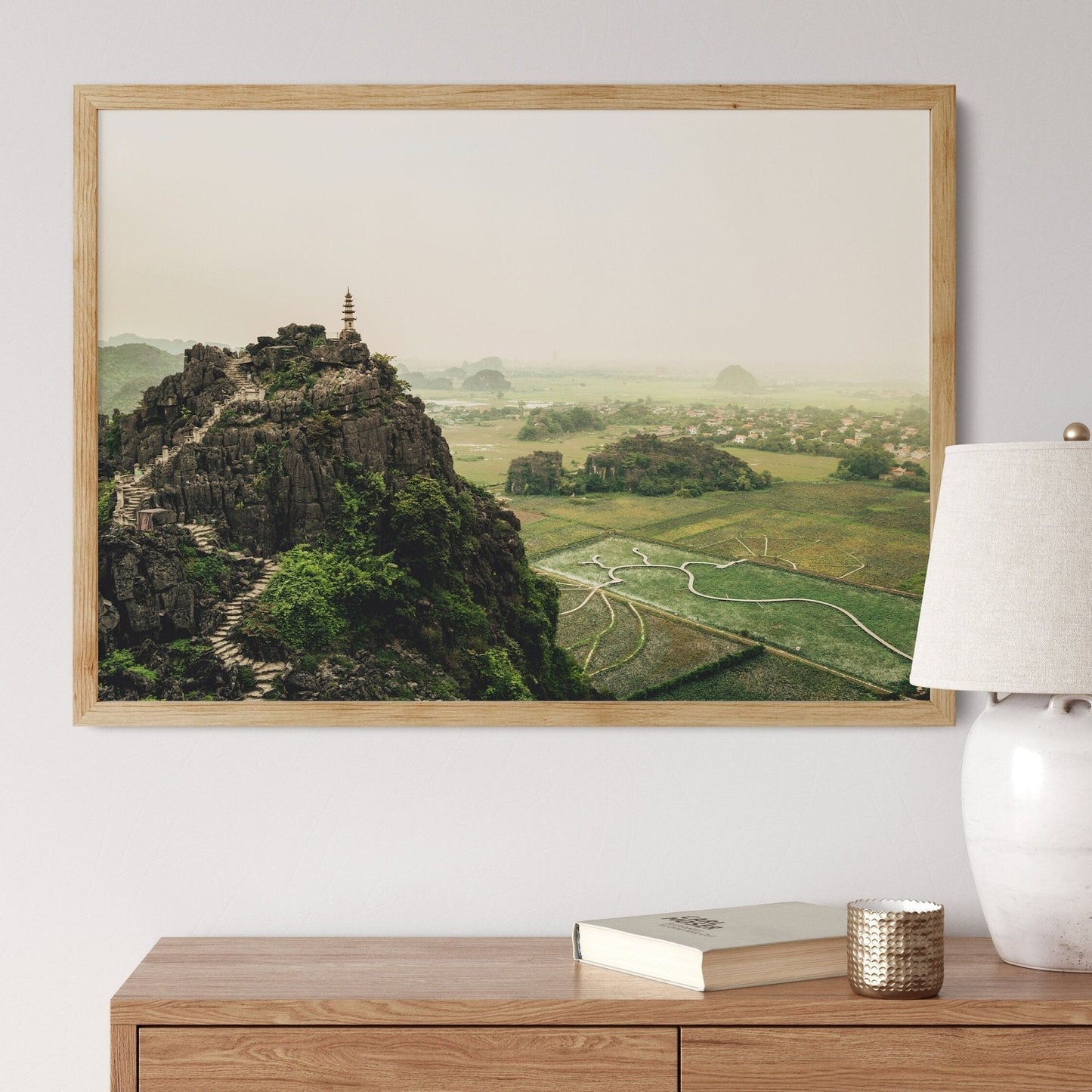 Hang Mua Peak II photo hanging above a wooden dresser shows a hill with steps, a tower, and green fields.