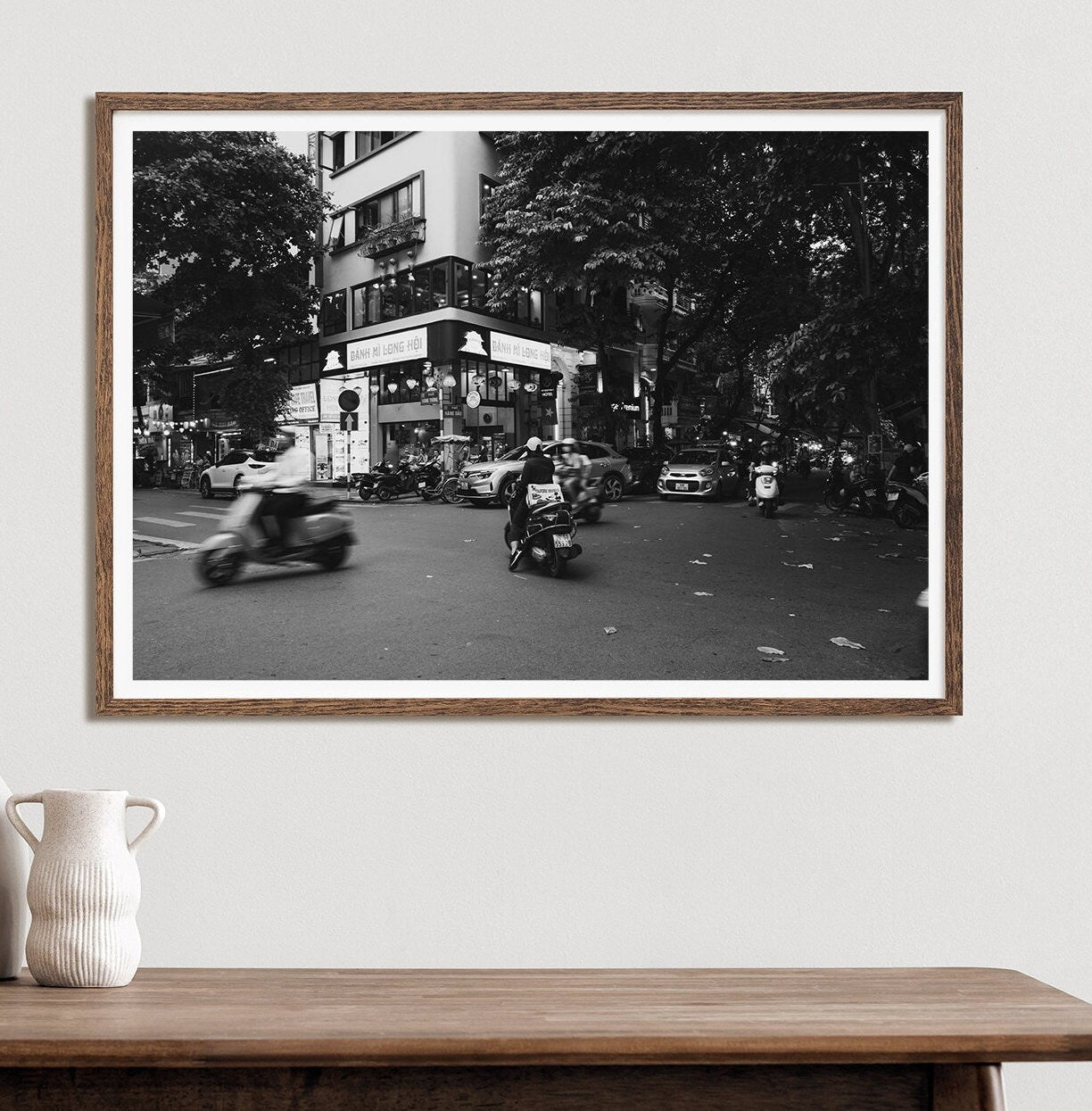 Hanoi Intersection Black and White framed photo of a busy city street hangs above a table with a vase.