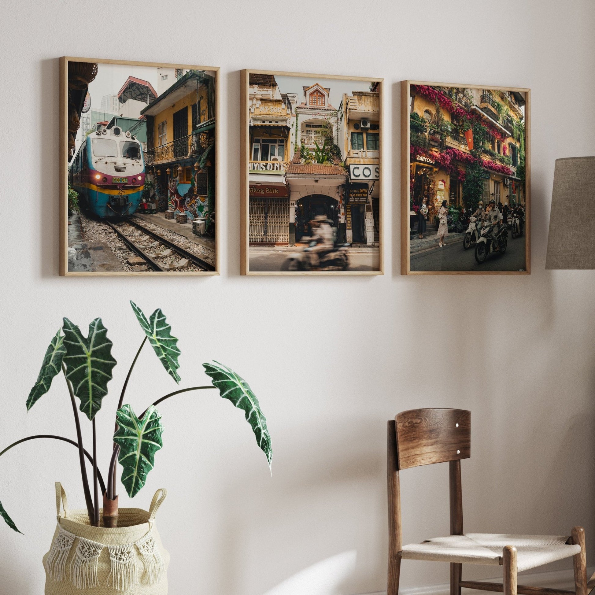 The Hanoi Streets - Set of 3 features framed photos of street scenes with bikes and flowers on a white wall above a chair.