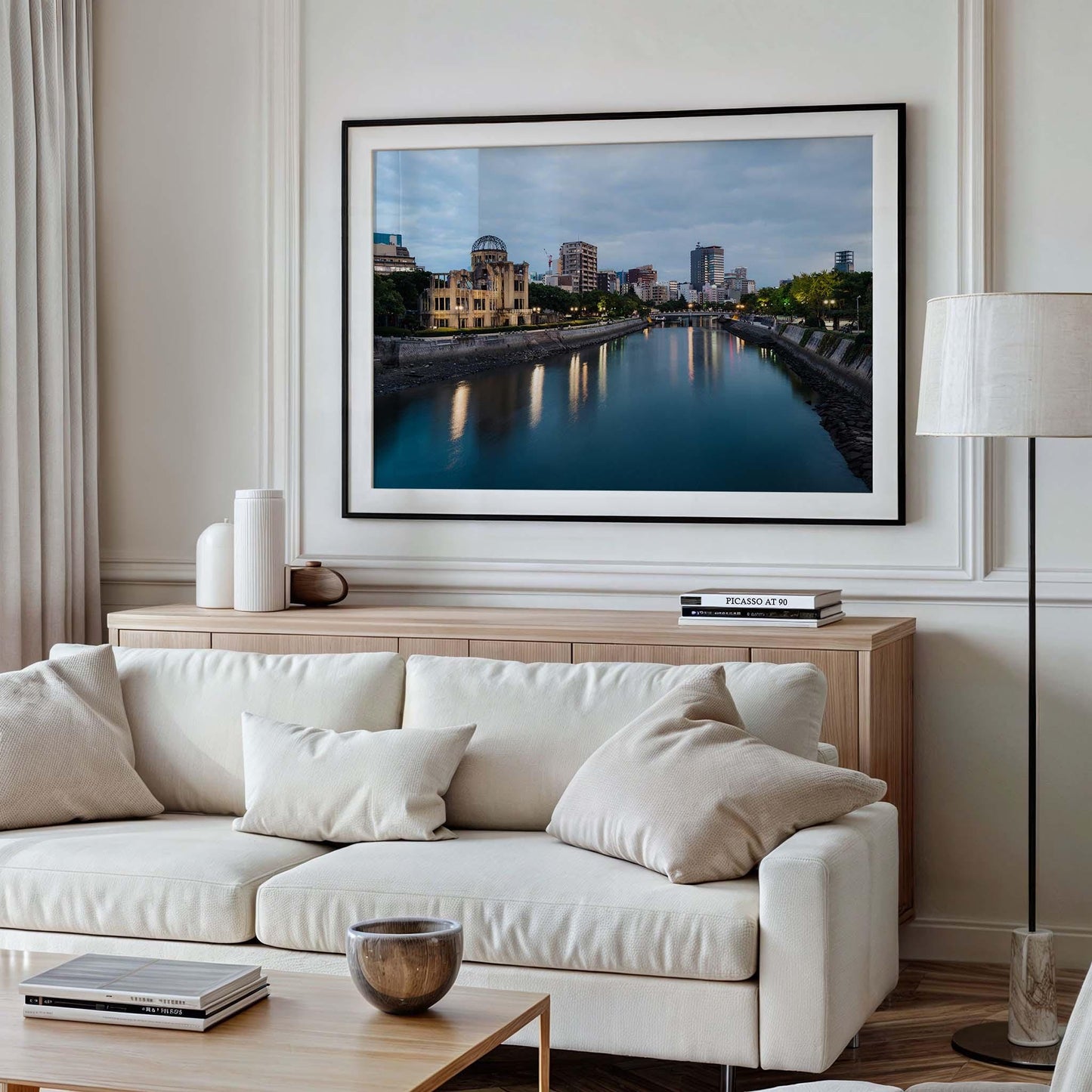 The Hiroshima Peace Memorial is framed above a white sofa with cushions, flanked by curtains and a floor lamp, in a modern living room.