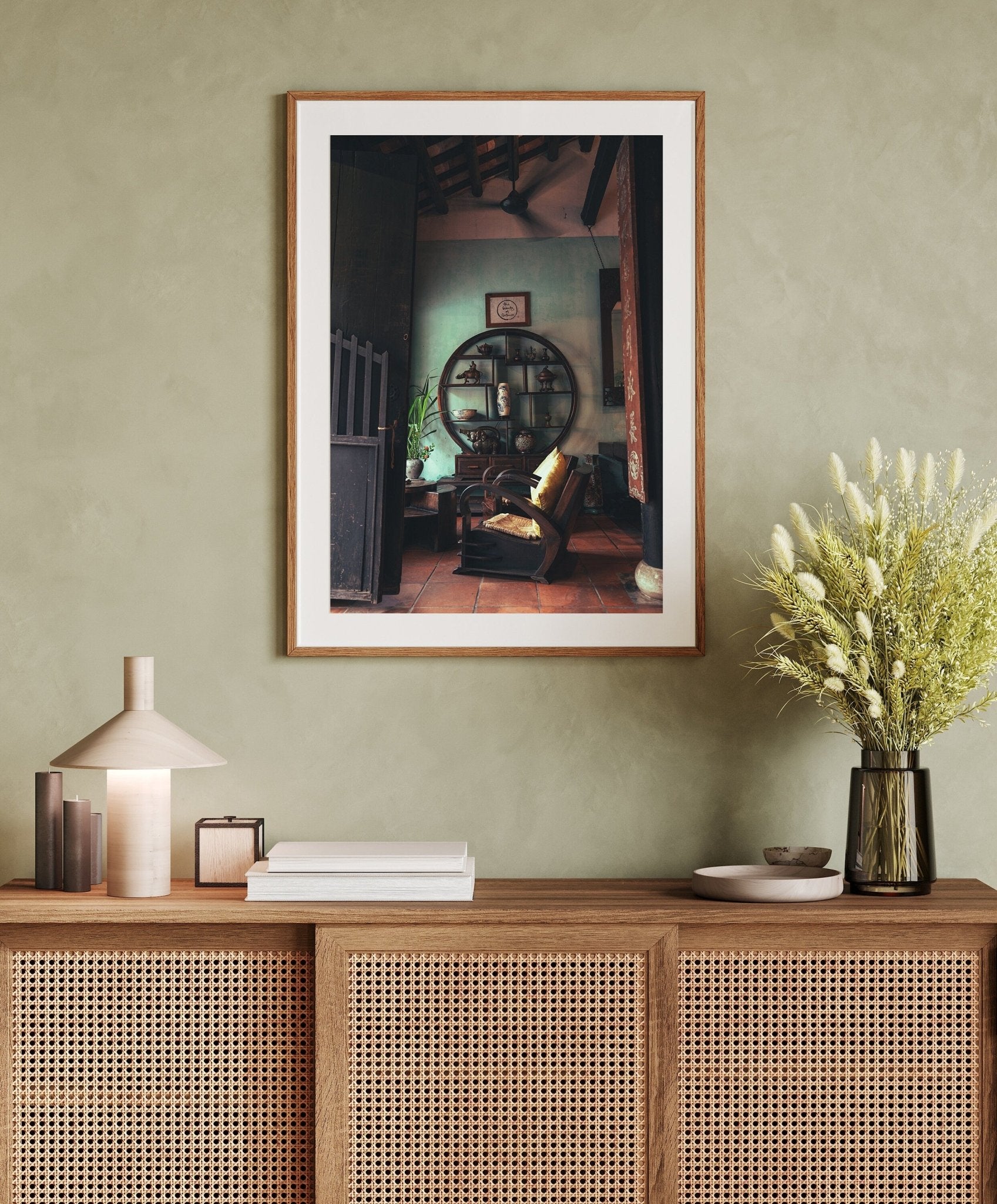 A cozy living room featuring Hoi An Tea Shop framed art on a wooden cabinet with a lamp, books, and a floral vase.