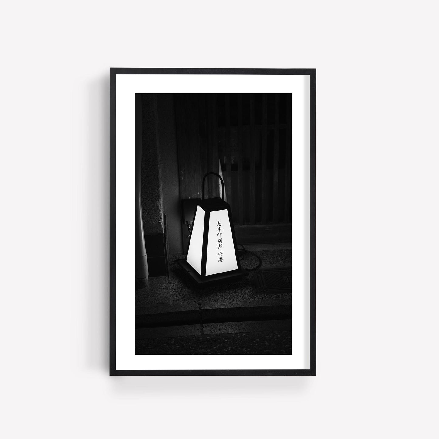 Part of the Japanese Cities Black and White set, this framed print shows a lantern with Japanese characters on a white wall.