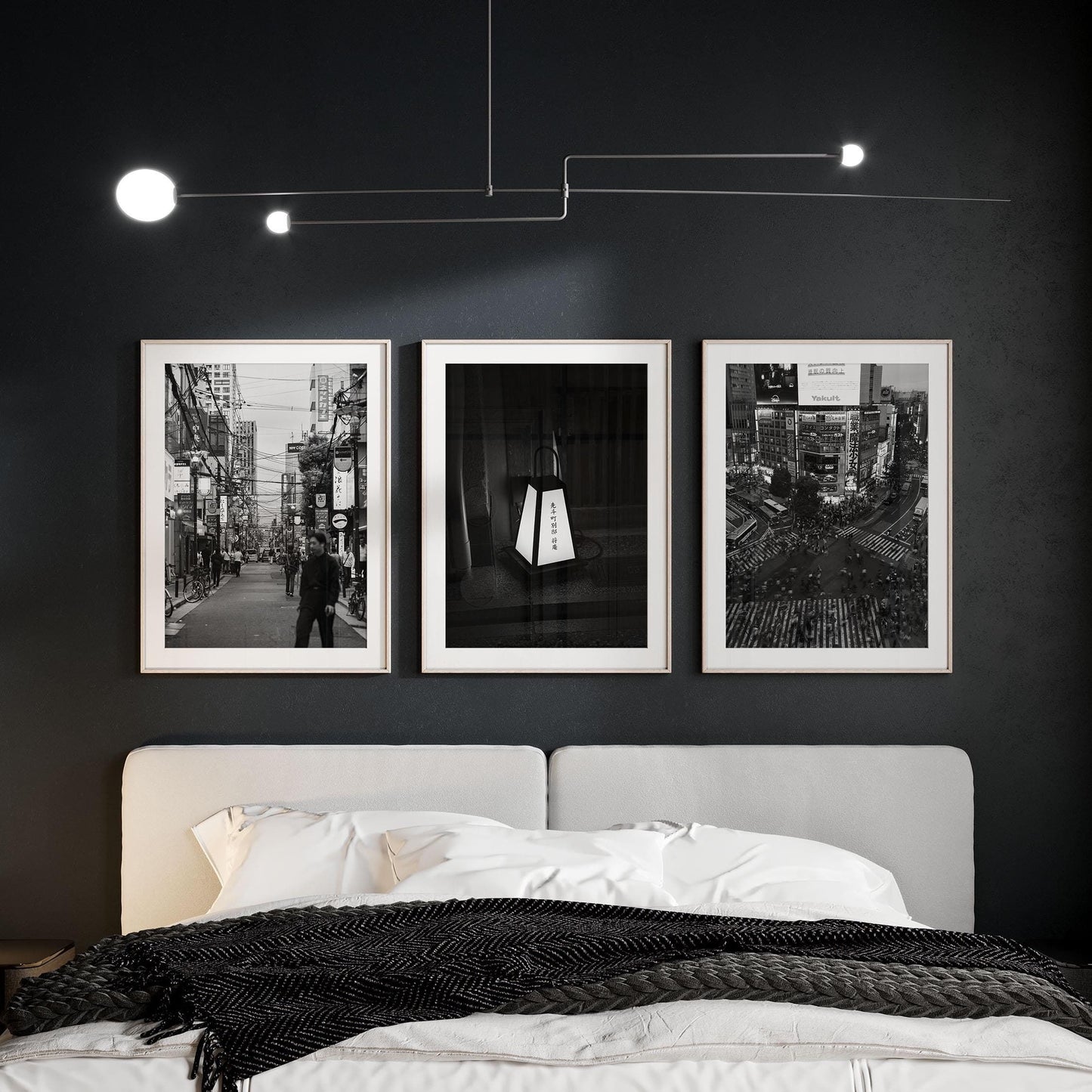 A bedroom with a gray bed, Japanese Cities Black and White set above the headboard, dark walls, and a modern ceiling light.