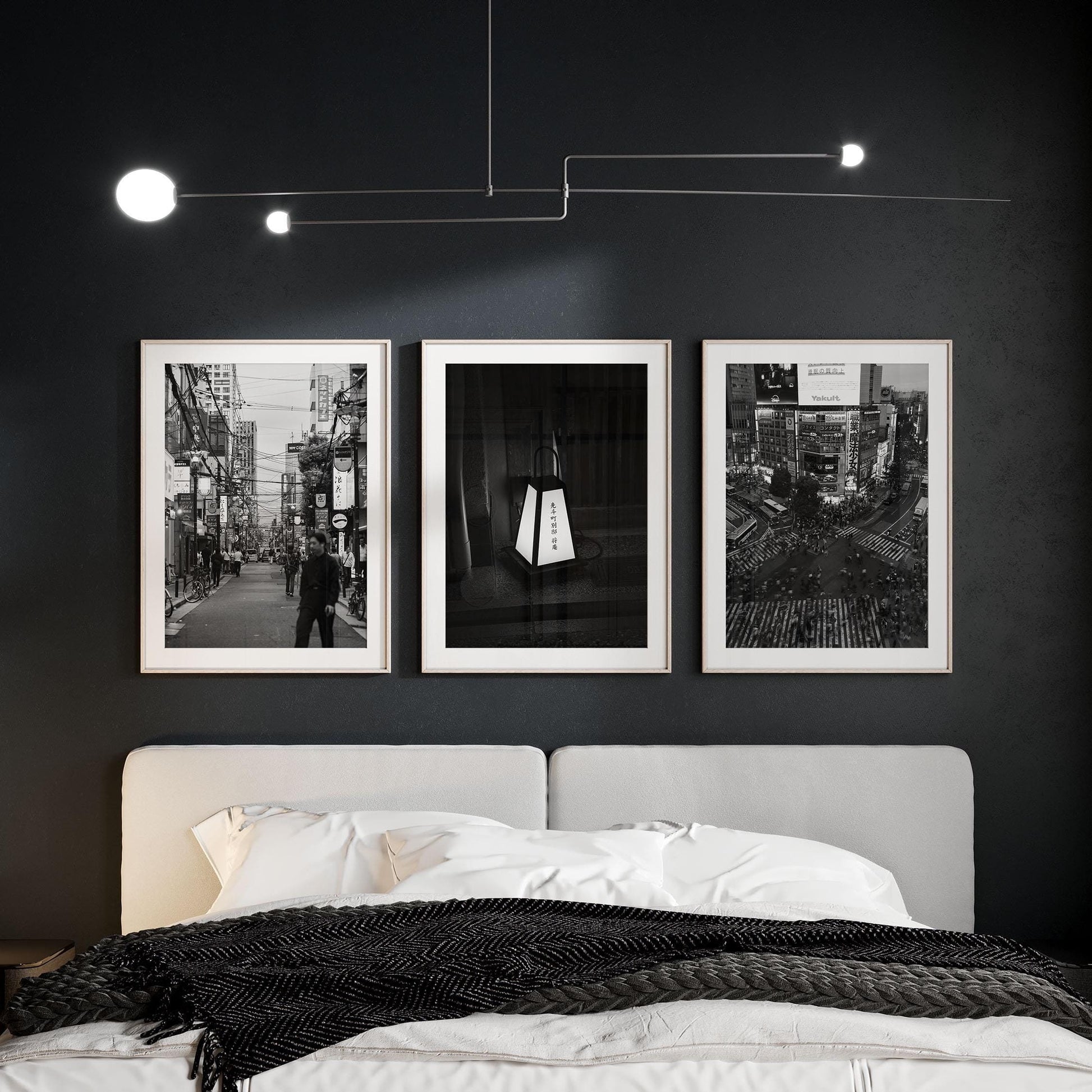 A bedroom with a gray bed, Japanese Cities Black and White set above the headboard, dark walls, and a modern ceiling light.