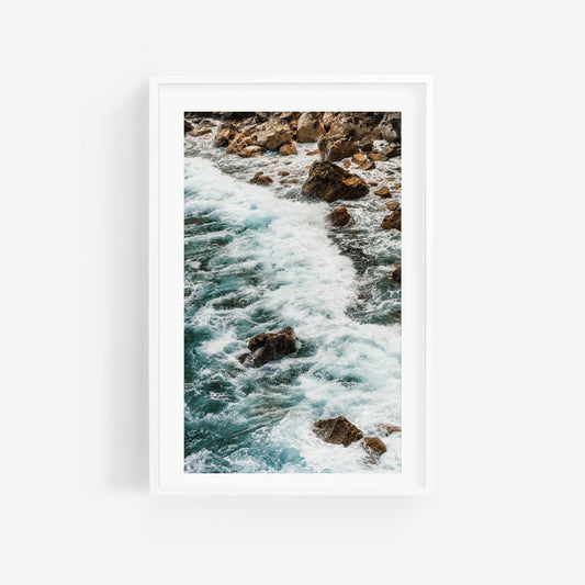 Teal Tide: A framed photo of ocean waves crashing on rocks, displayed on a white wall.