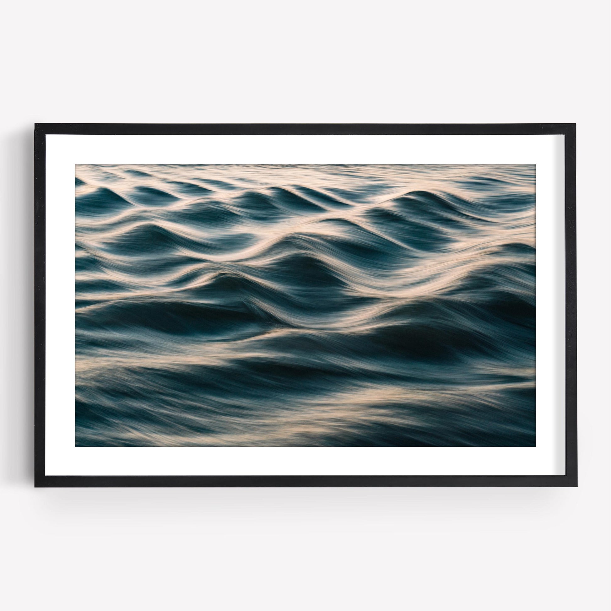 “Silk Waves” abstract photo of rippling ocean with soft golden light, in a sleek black and white frame.