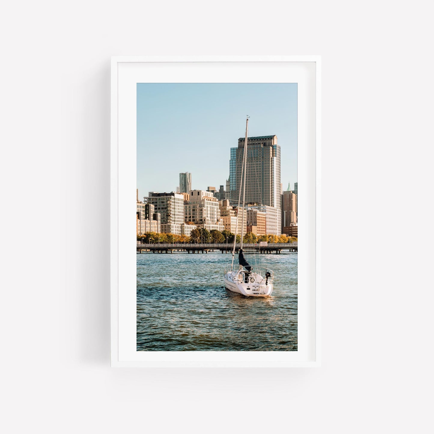 Tribeca Waters sailboat glides on water with city skyscrapers in the background under a clear blue sky.
