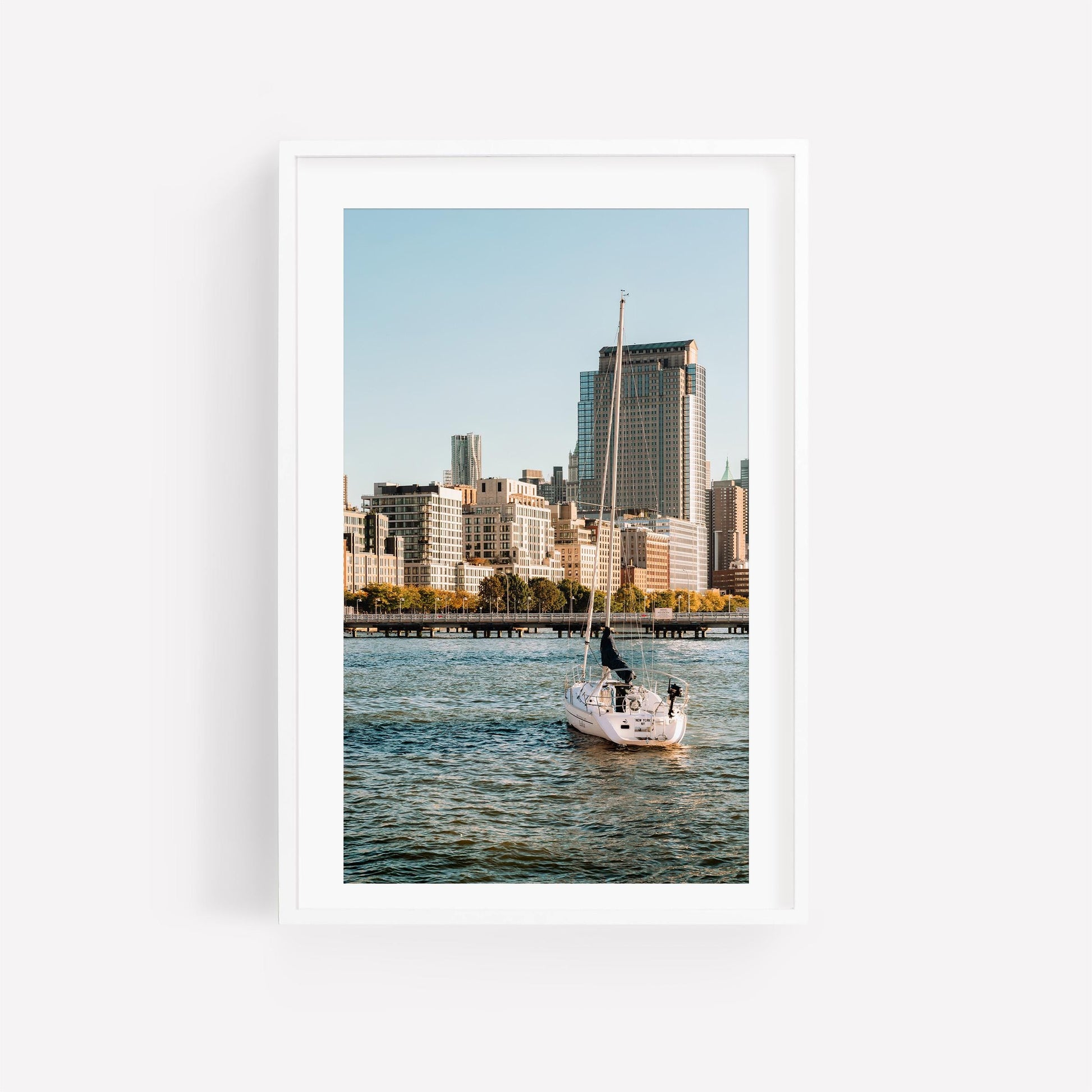 Tribeca Waters sailboat glides on water with city skyscrapers in the background under a clear blue sky.