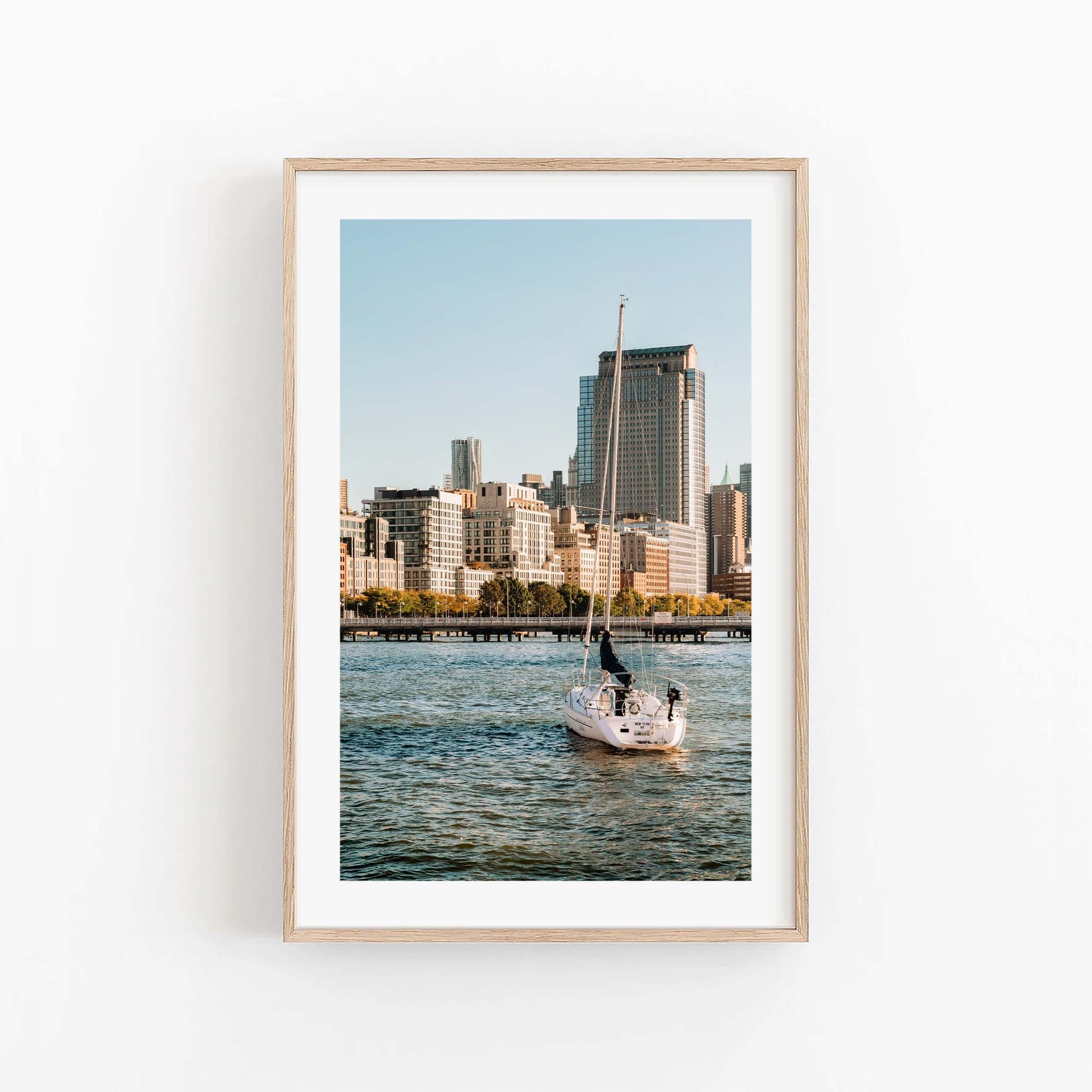 Tribeca Waters" framed photo of a sailboat with a city skyline, displayed on a white wall.