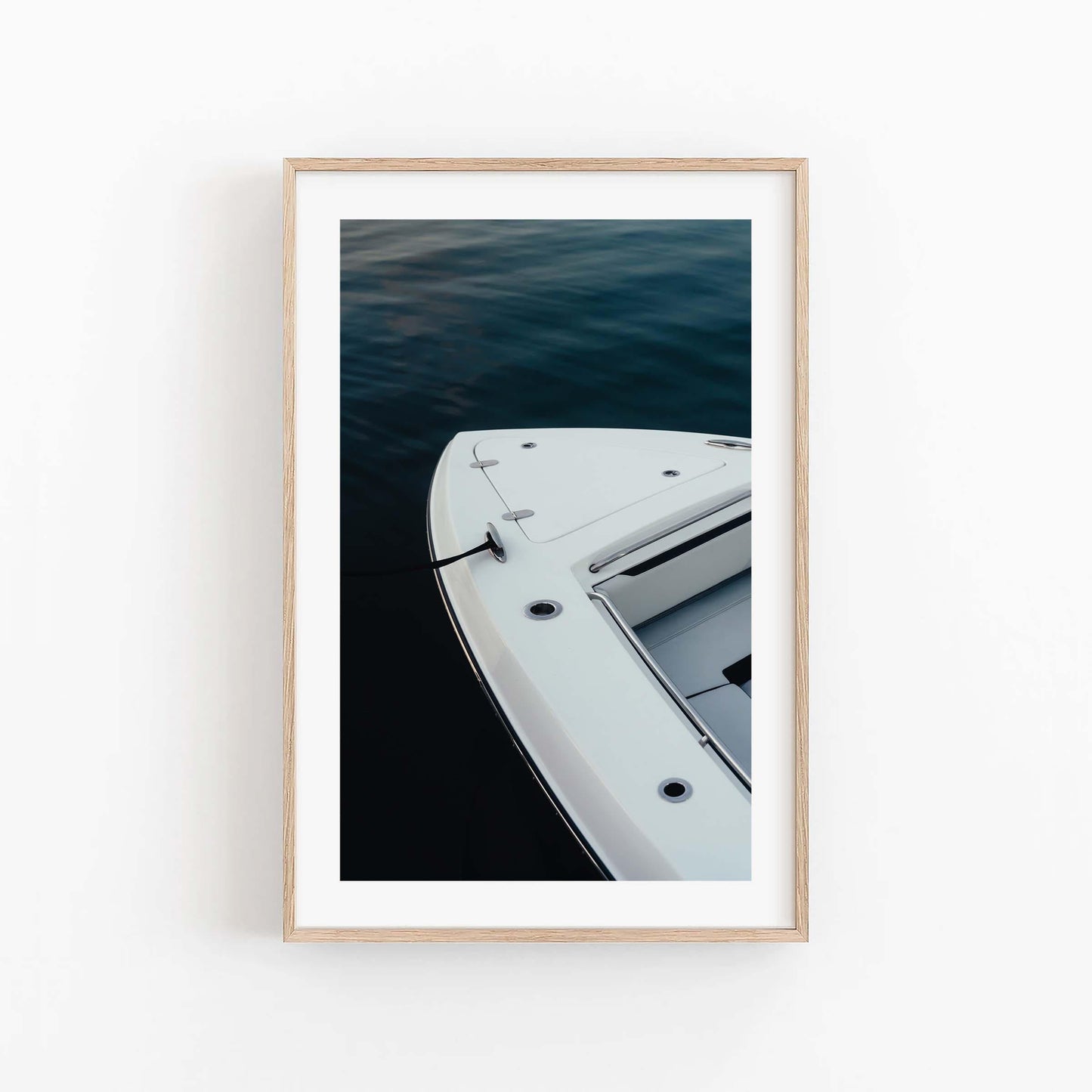 Blue Hour Mooring“ framed photo shows a boat’s bow on dark water, viewed from above against a white wall.