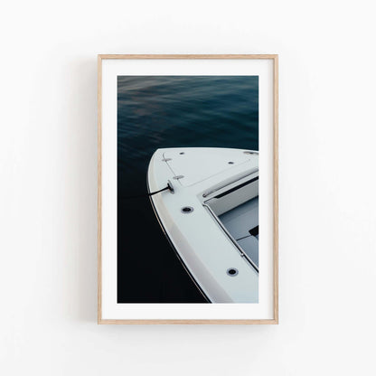 Blue Hour Mooring“ framed photo shows a boat’s bow on dark water, viewed from above against a white wall.