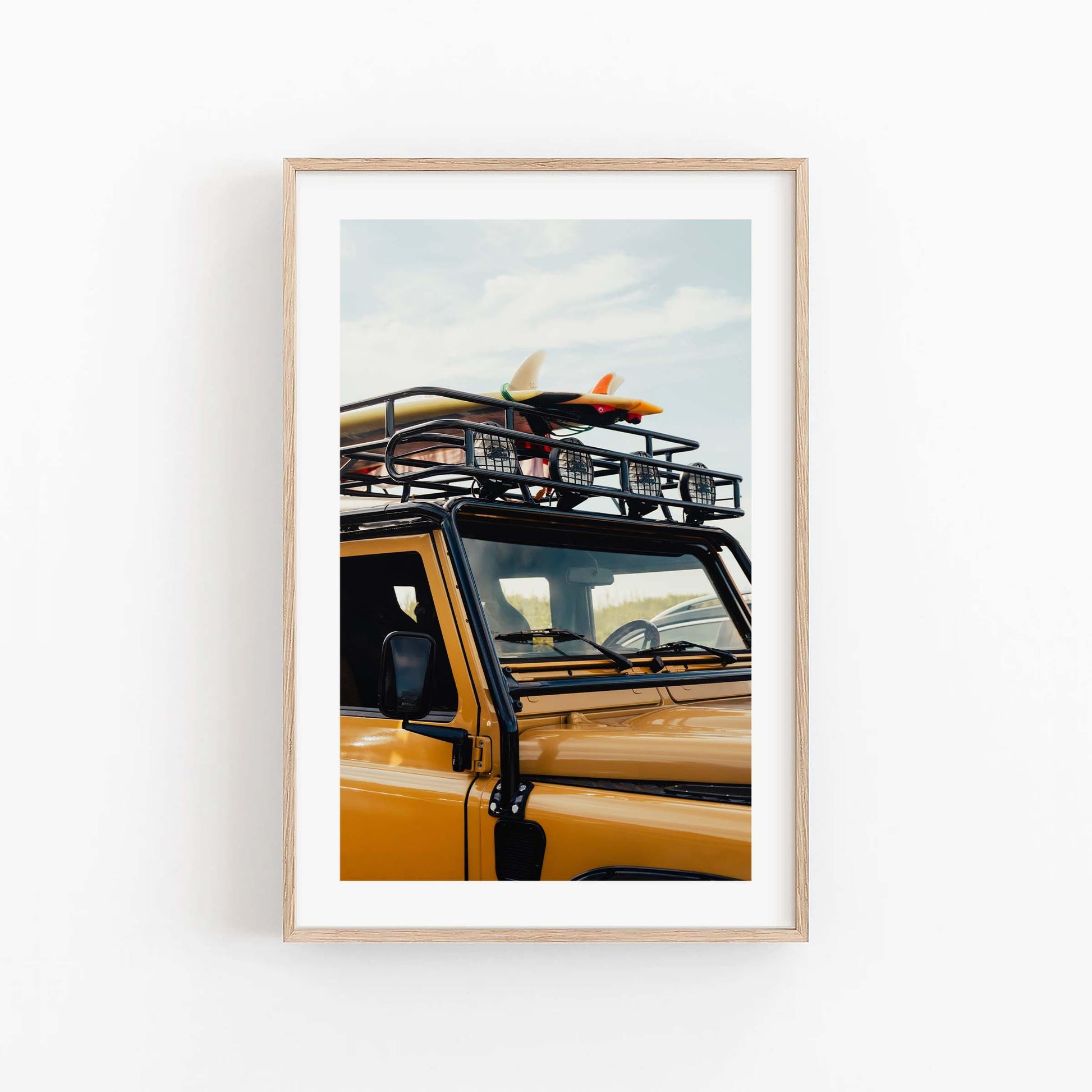 Photo of Surf Roadtrip: yellow SUV with surfboard on roof rack, light wood frame, against a white wall.
