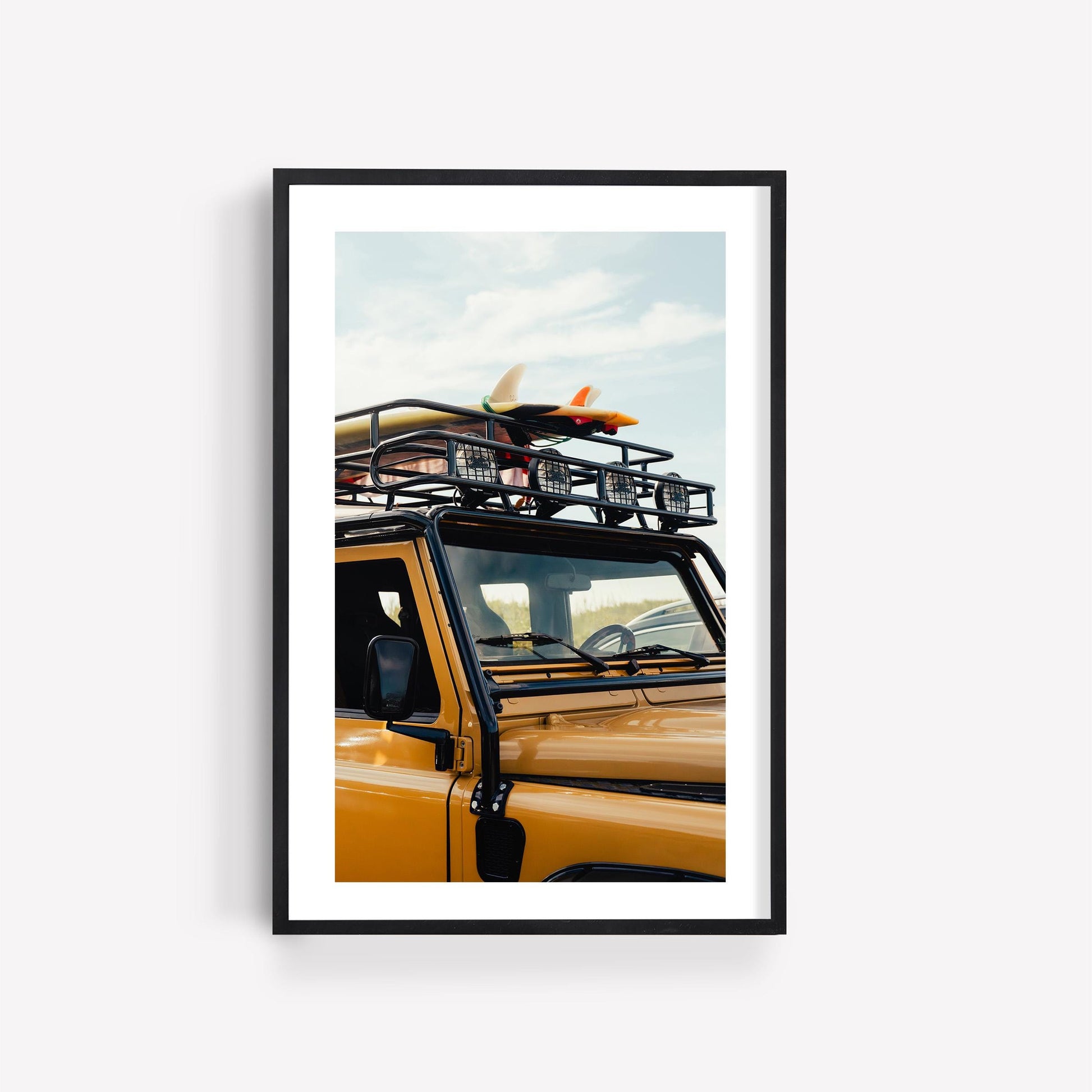 Framed “Surf Roadtrip” photo: yellow SUV with surfboards on the roof, set against a clear blue sky.