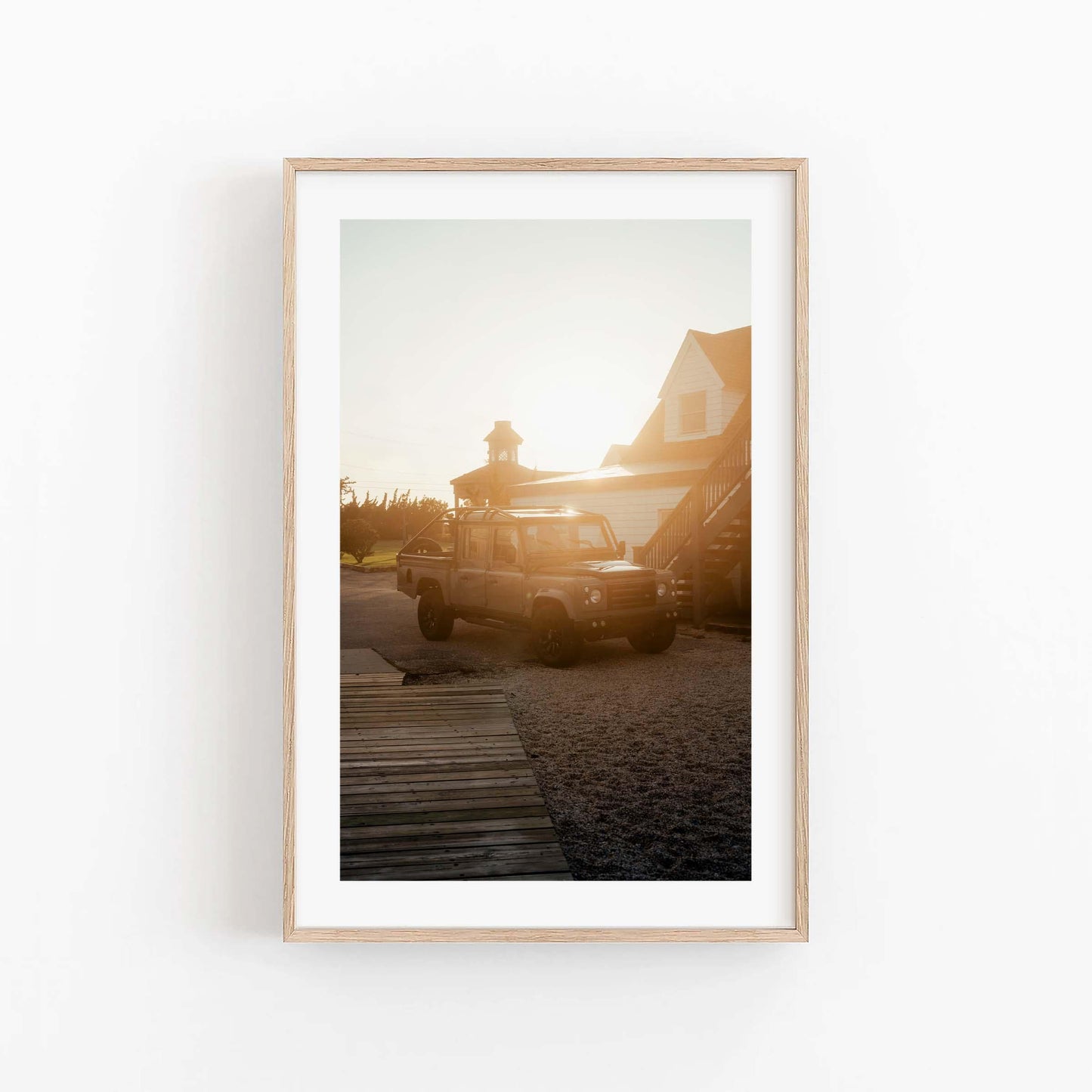 Golden Hour Defender framed photo: parked SUV at sunset near house, displayed on plain white wall.