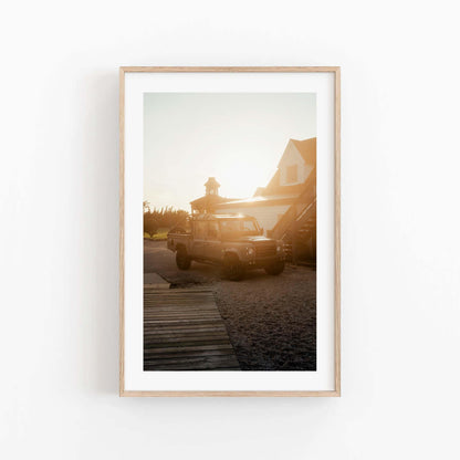 Golden Hour Defender framed photo: parked SUV at sunset near house, displayed on plain white wall.