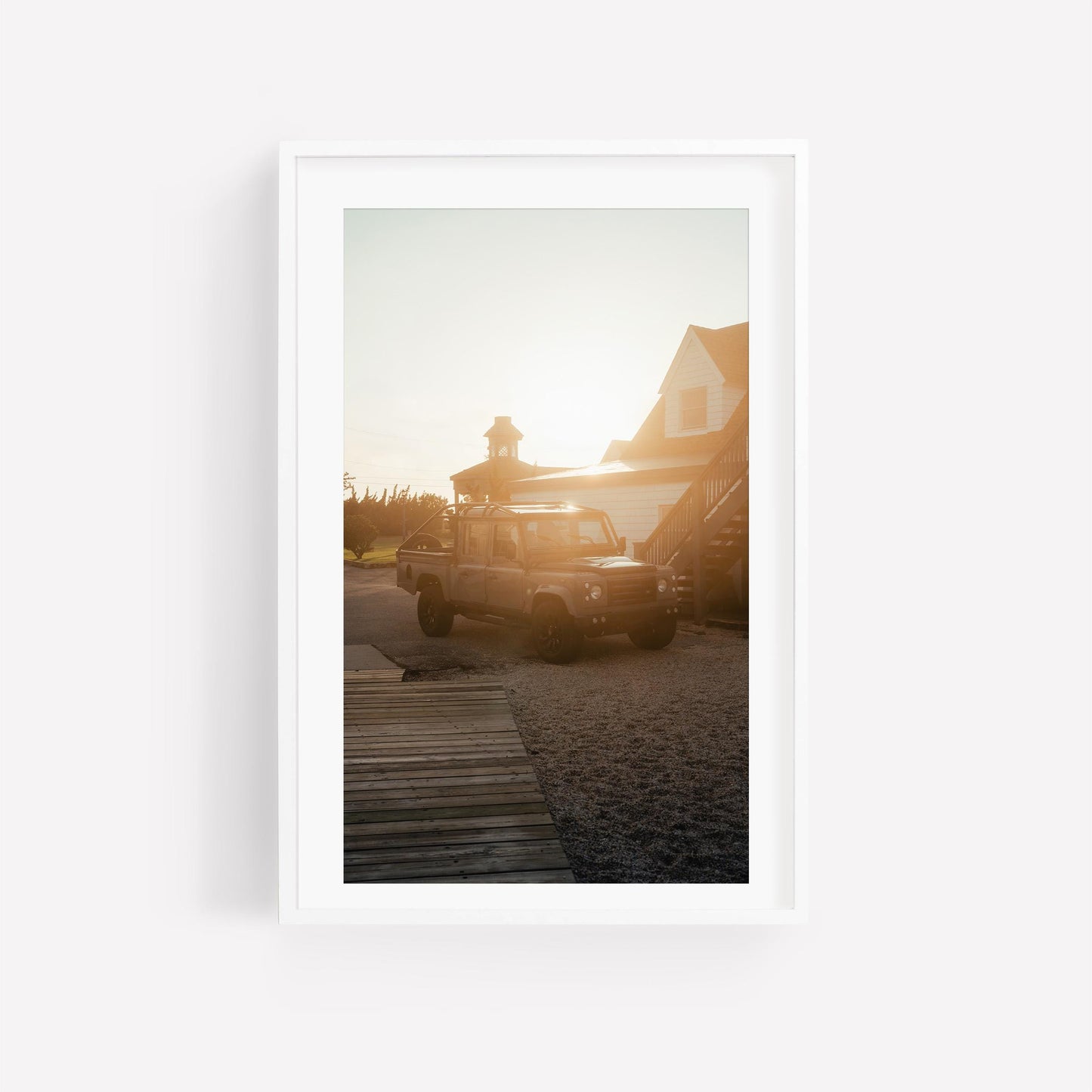 Golden Hour Defender SUV by a house at sunset, light aglow behind the roof, wooden path in front.