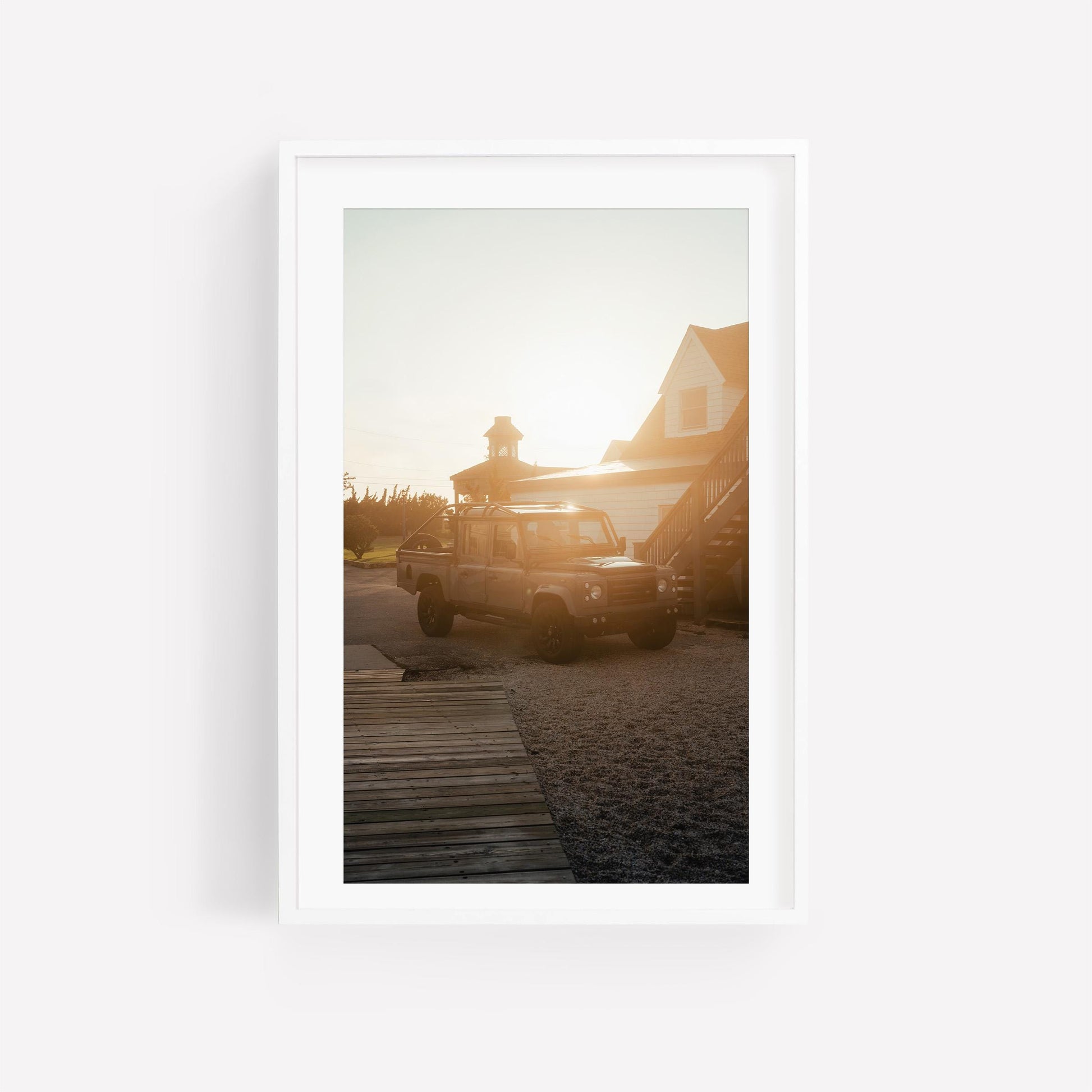 Golden Hour Defender SUV by a house at sunset, light aglow behind the roof, wooden path in front.