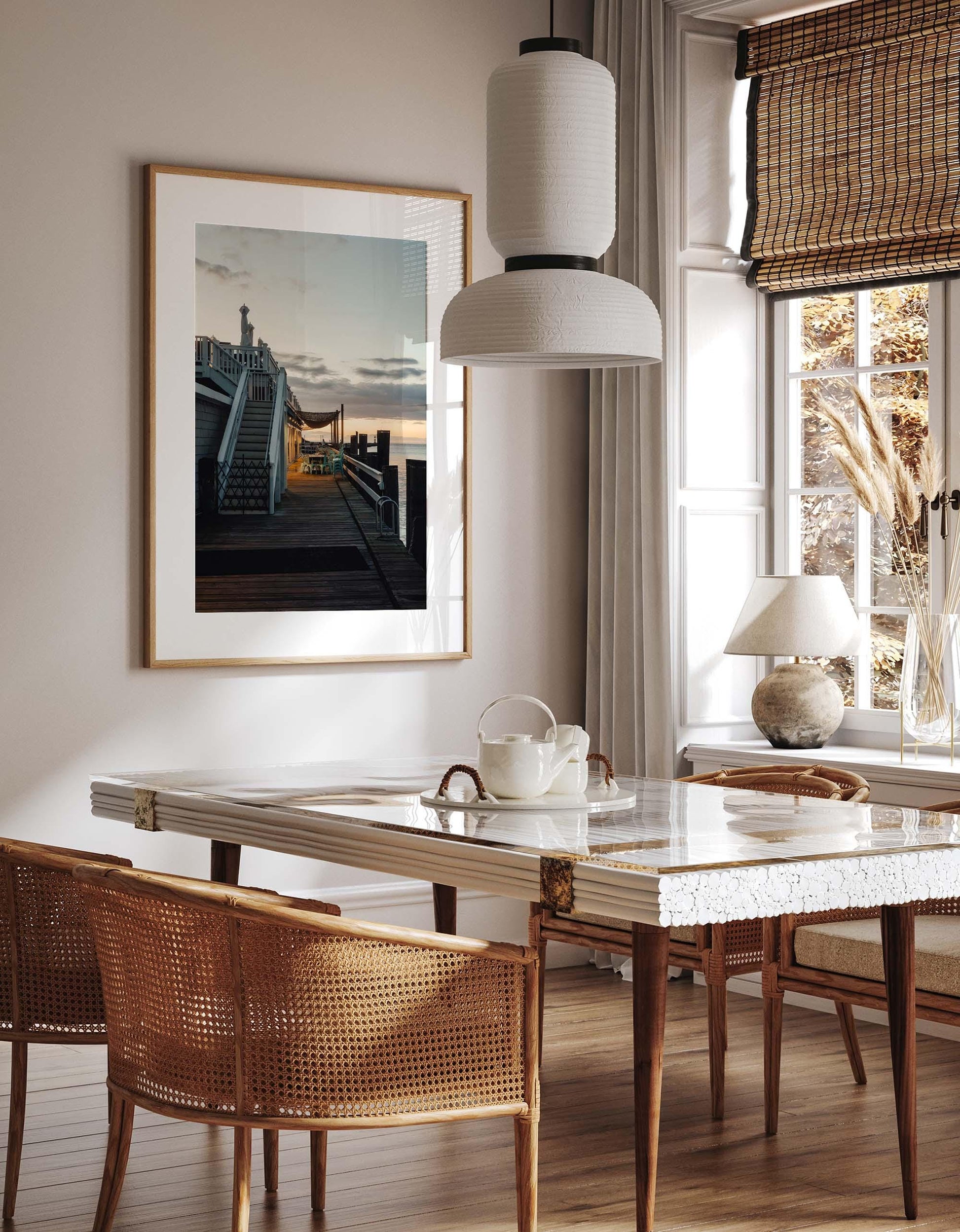 Bright dining room with a marble table, wicker chairs, and “Dockside Evening” framed on the wall.