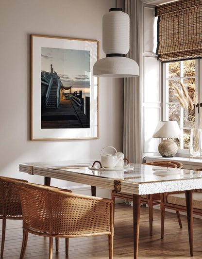 Bright dining room with a marble table, wicker chairs, and “Dockside Evening” framed on the wall.