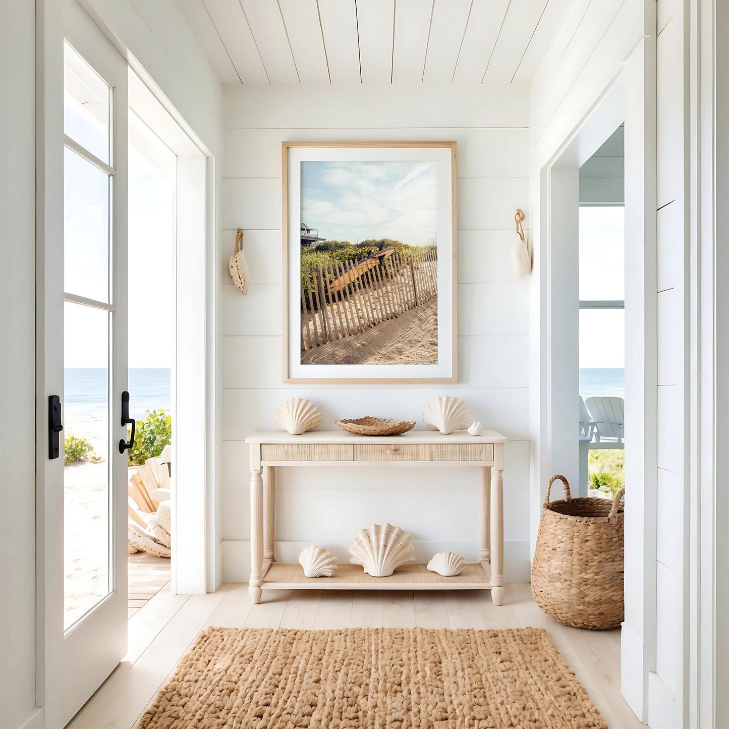 Bright coastal entryway with seashells, woven rug, basket, and Ditch Plains Surfboard above a light wood console table.