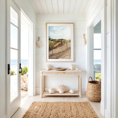 Bright coastal entryway with seashells, woven rug, basket, and Ditch Plains Surfboard above a light wood console table.