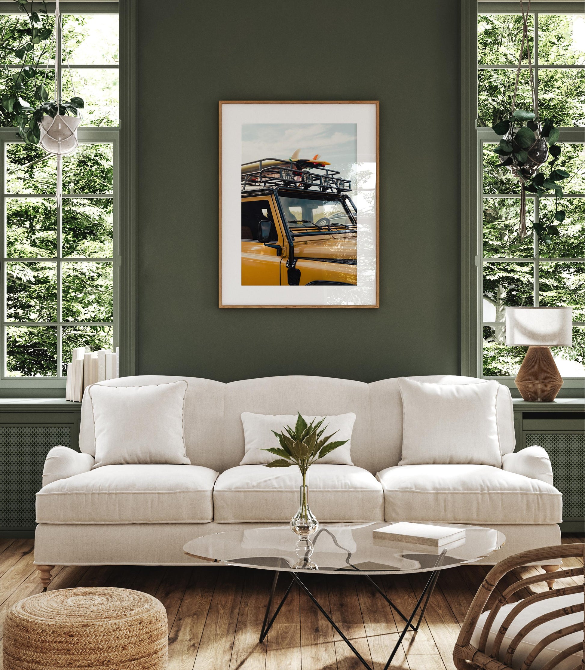 A white sofa sits in a green room with large windows and Surf Roadtrip art framed on the wall above it.