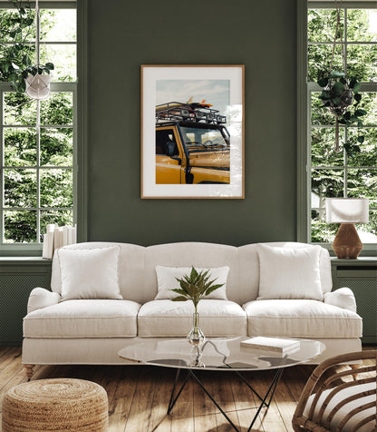 A white sofa sits in a green room with large windows and Surf Roadtrip art framed on the wall above it.