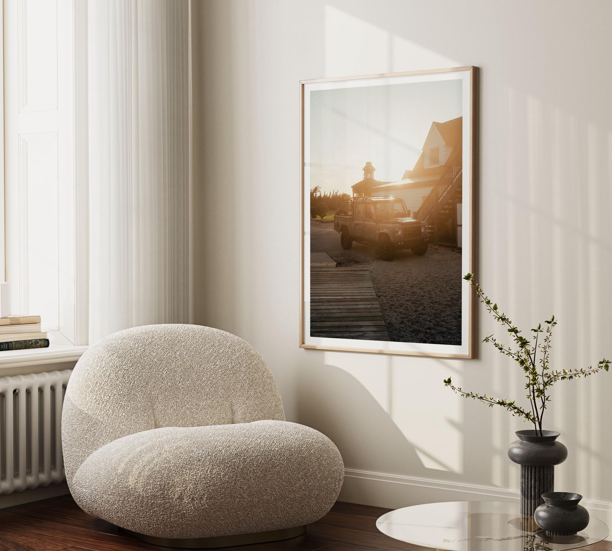 Golden Hour Defender chair by a window, beside a plant and round table, with car and house art on the wall.
