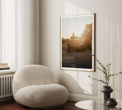 Golden Hour Defender chair by a window, beside a plant and round table, with car and house art on the wall.