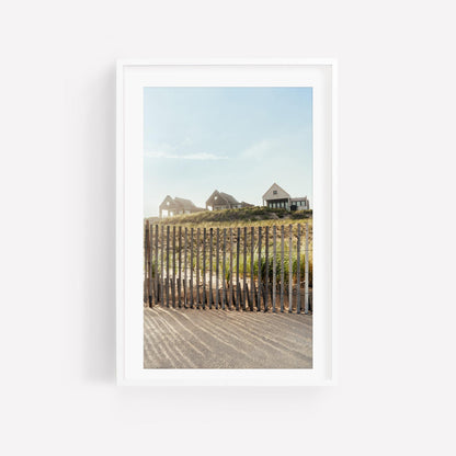Summer Homes: Three houses on a grassy hill behind a fence under blue sky, framed in white.