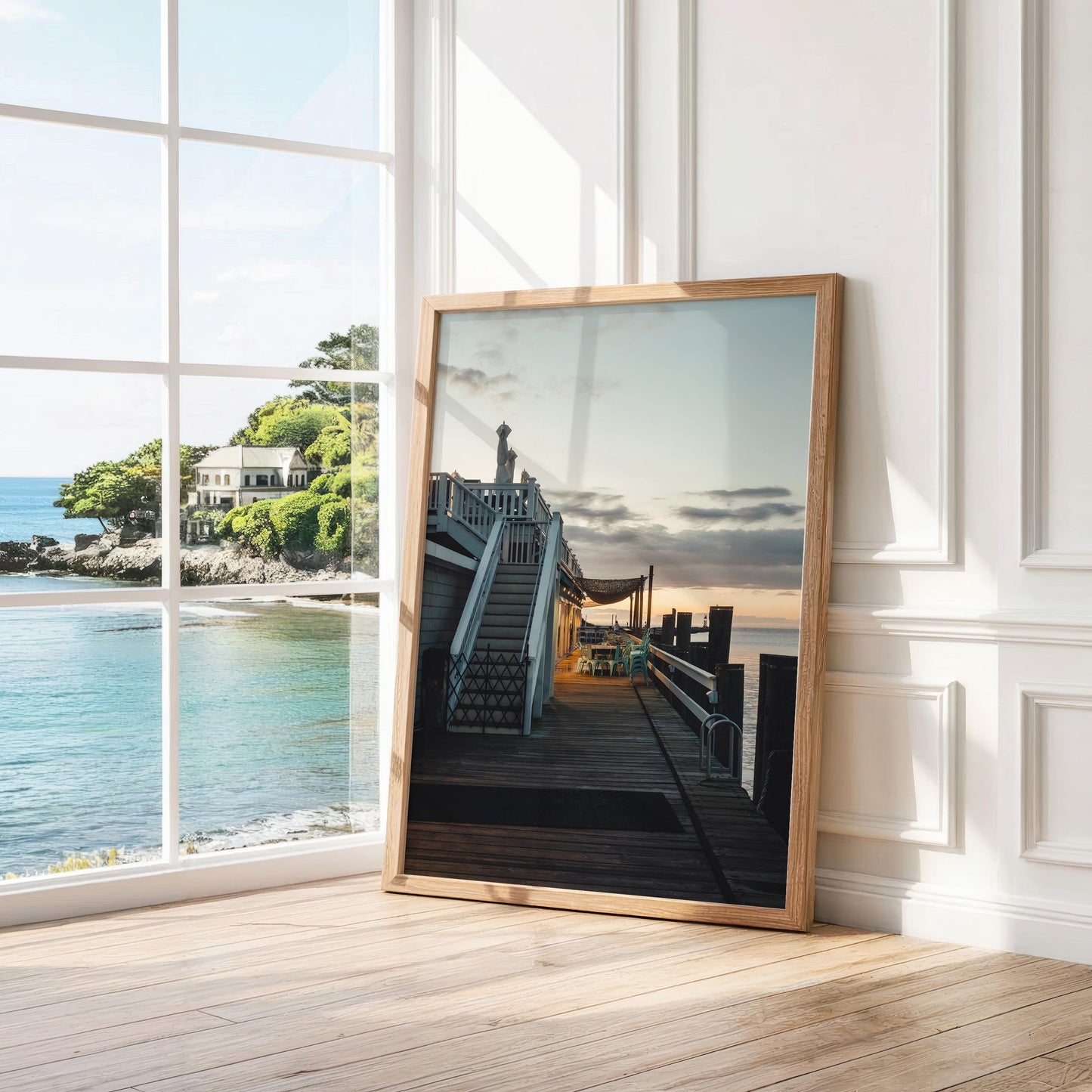 Dockside Evening framed photo leans by a window, showcasing an ocean view with houses outside.