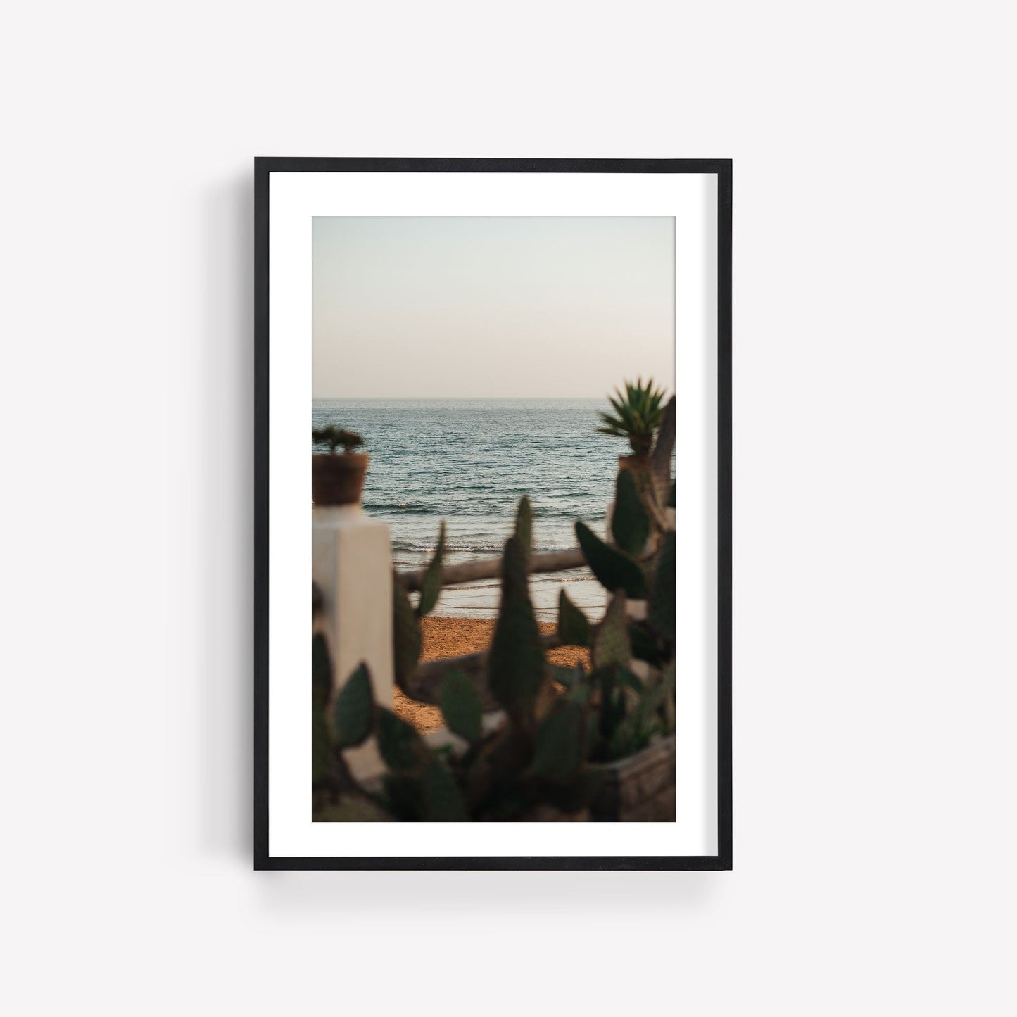 Experience In the Distance, a framed picture capturing a tranquil beach with cactus plants and a calm sea.