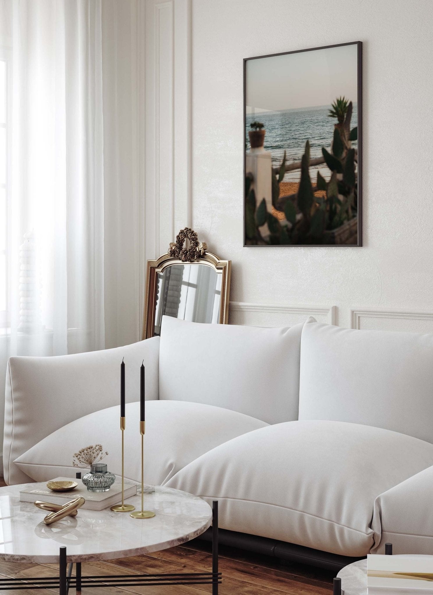 A cozy living room with a white sofa, marble table, candles, and In the Distance wall art. A mirror leans against the wall.