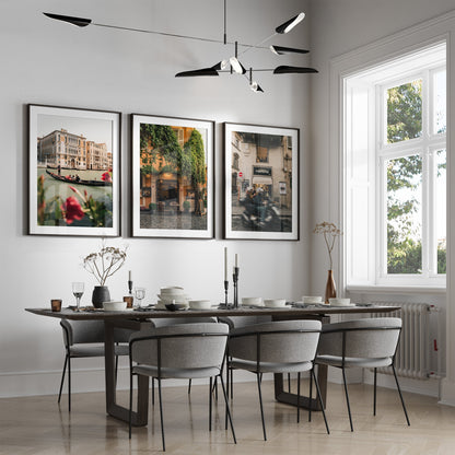Modern dining room with six gray chairs, dark table, Italy - Set of 3 wall art, and a large window with natural light.