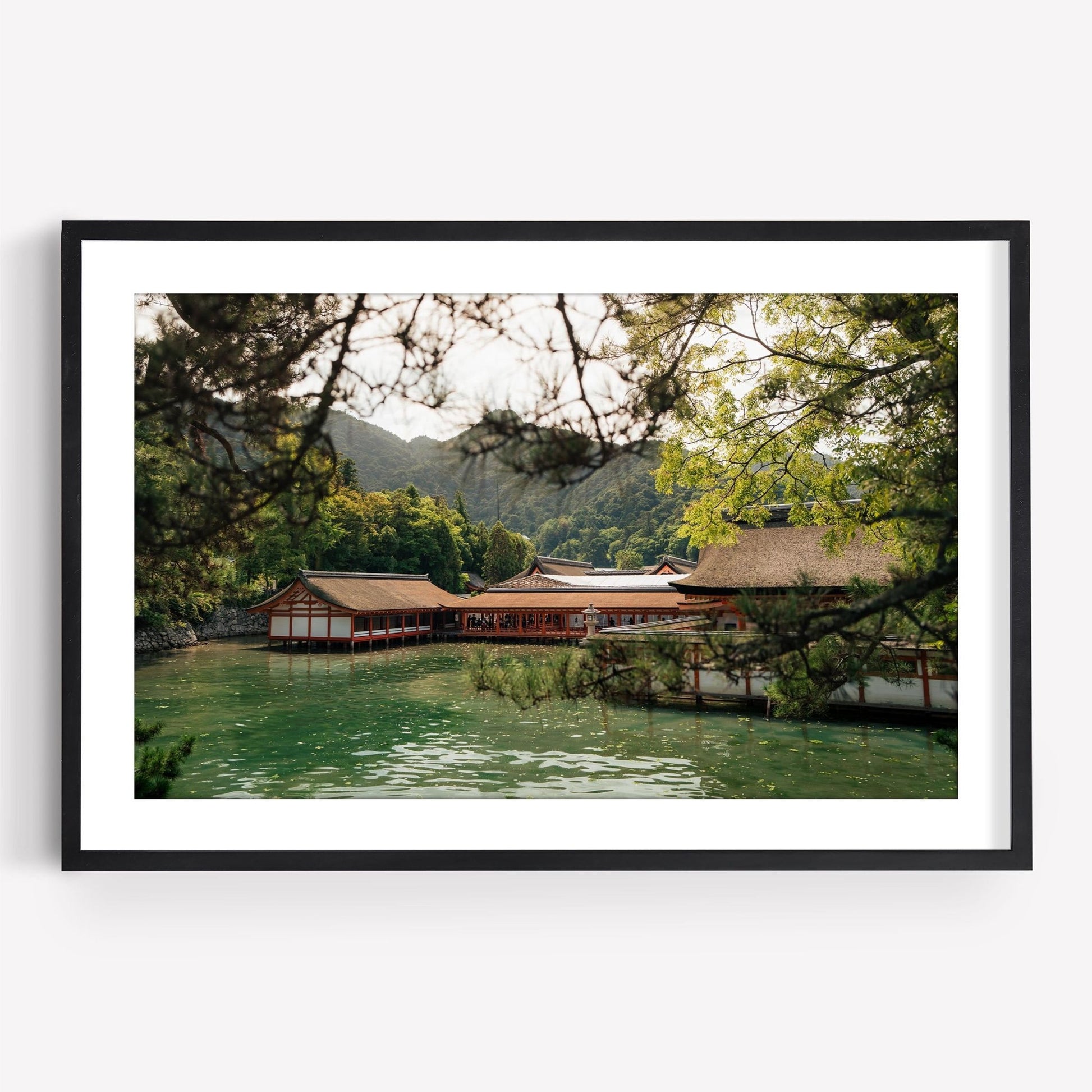 Framed photo titled Itsukushima Shrine I, showcasing a traditional Japanese building over water, surrounded by trees and mountains.