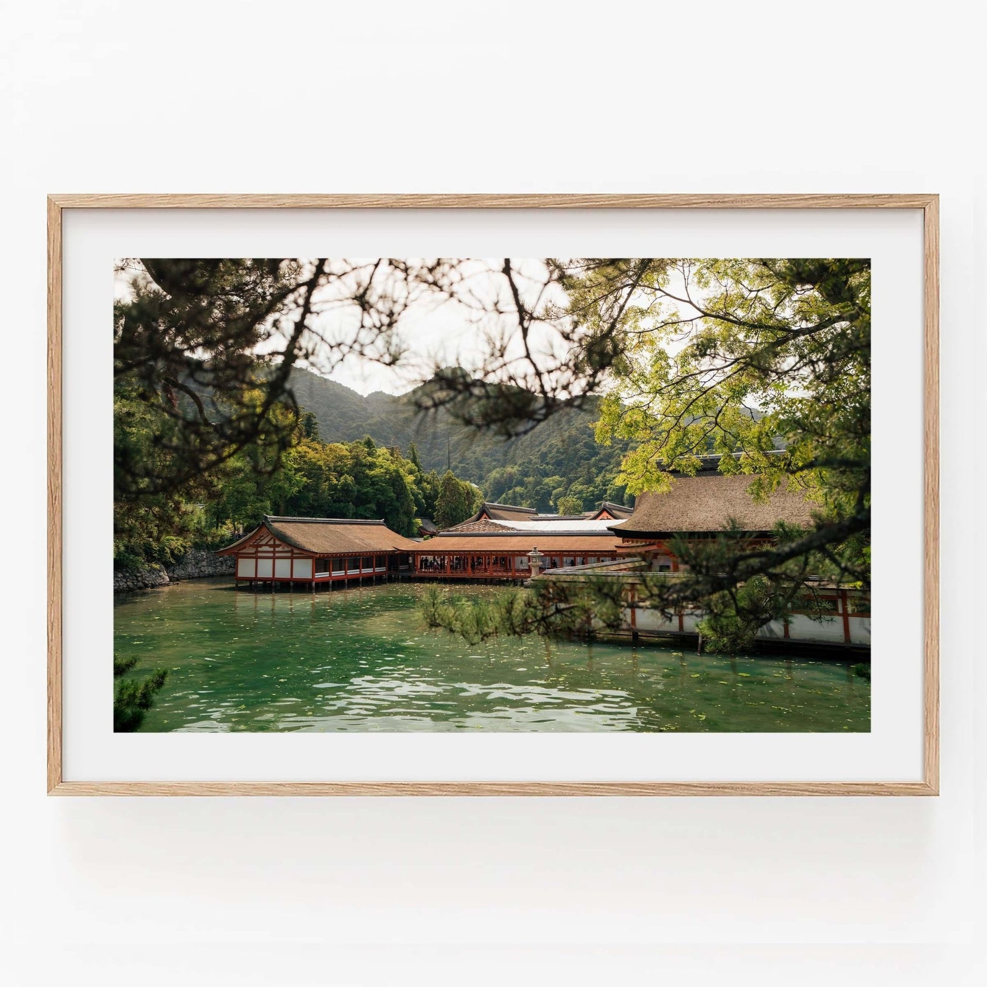 Framed photo of the Itsukushima Shrine I, depicting a serene Japanese temple by a lake with surrounding trees and mountains.