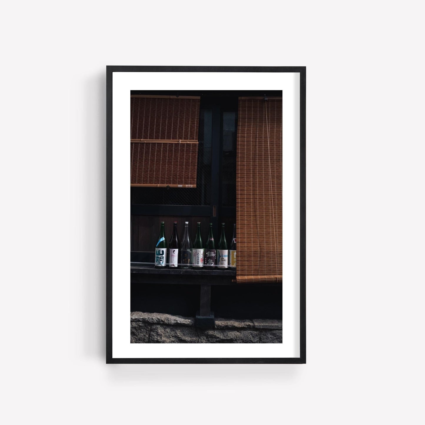 Framed photo titled Japanese Serenity - Set of 3 features sake bottles lined up under bamboo blinds against a dark background.