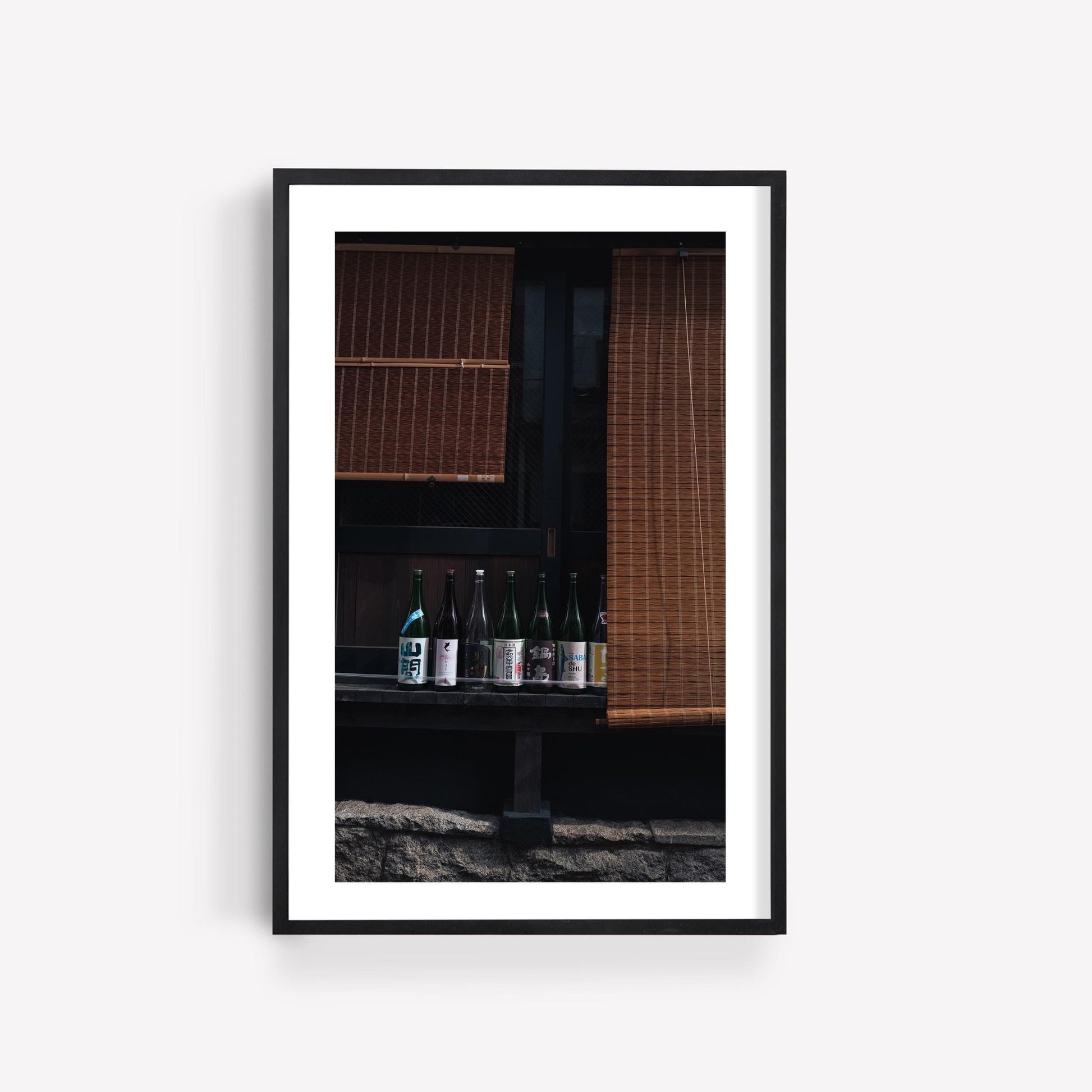 Framed photo titled Japanese Serenity - Set of 3 features sake bottles lined up under bamboo blinds against a dark background.