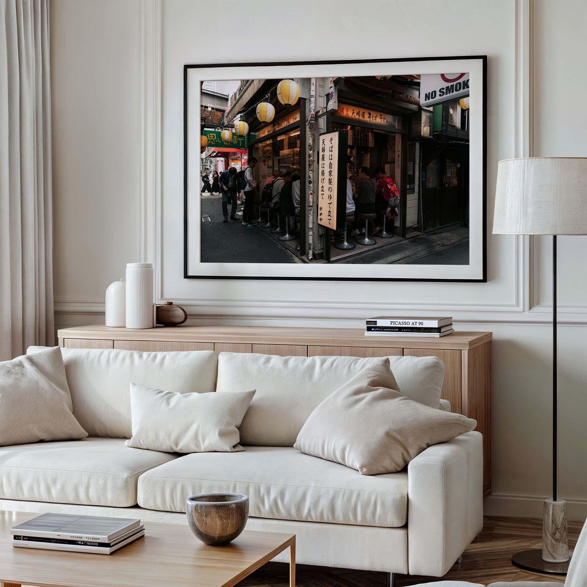 A cozy living room featuring a white Kameya Soba sofa, pillows, and a framed street scene photo on the wall above a sideboard.