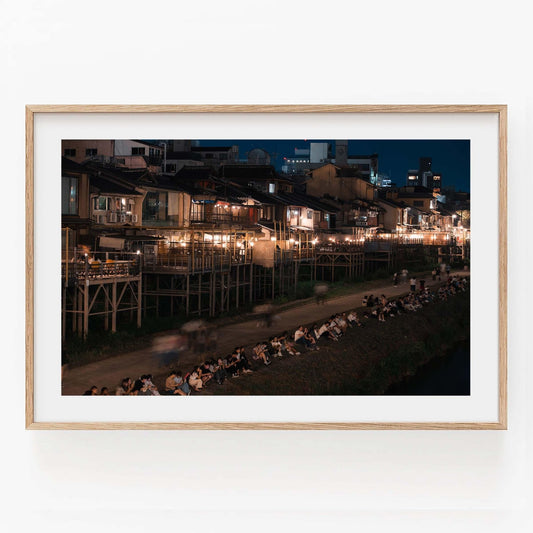 Framed photo titled Kamo River depicting a bustling riverside street with people and lit buildings at night.